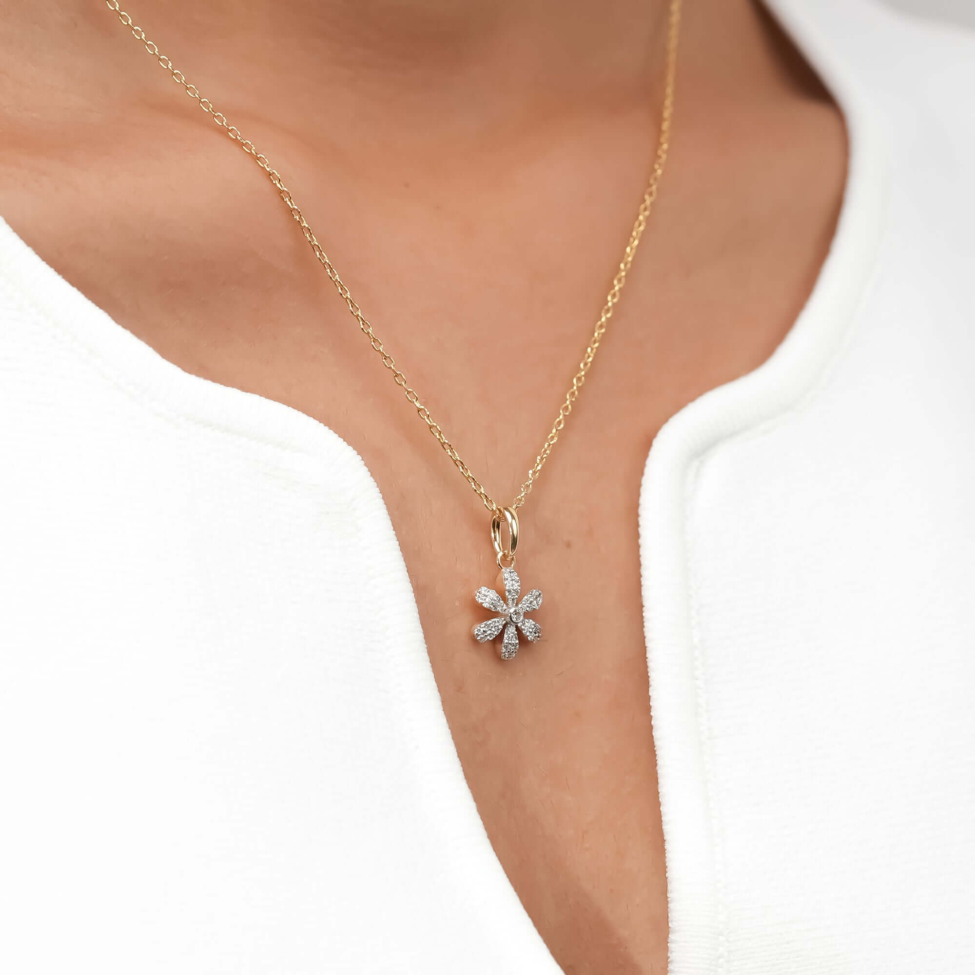 A dainty daisy pendant sparkles at the center of a gold chain, representing natural beauty and understated grace.