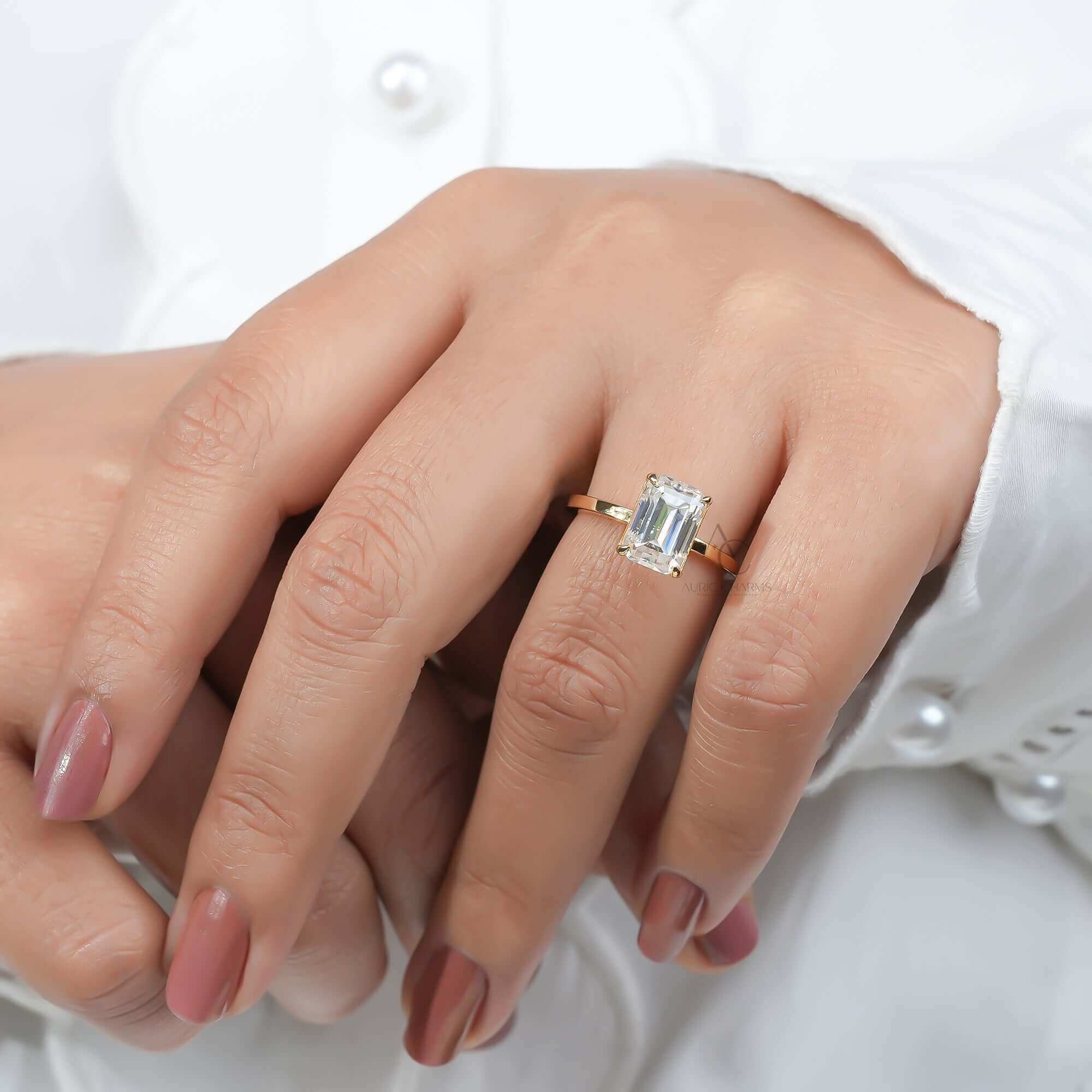 Emerald diamond solitaire ring on finger, minimal band.