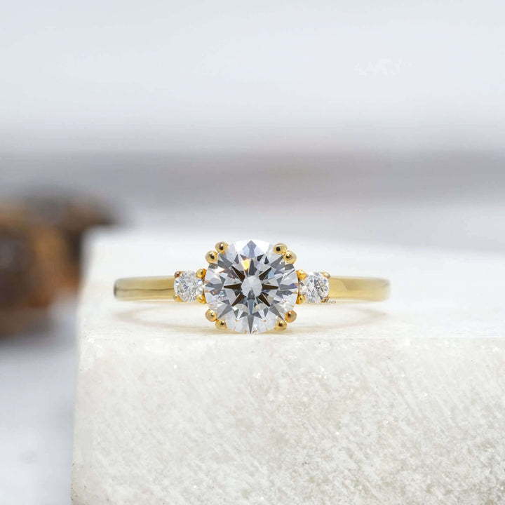 A stunning round-cut diamond engagement ring featuring a simple yet elegant band design, reflecting brilliance on a white surface.