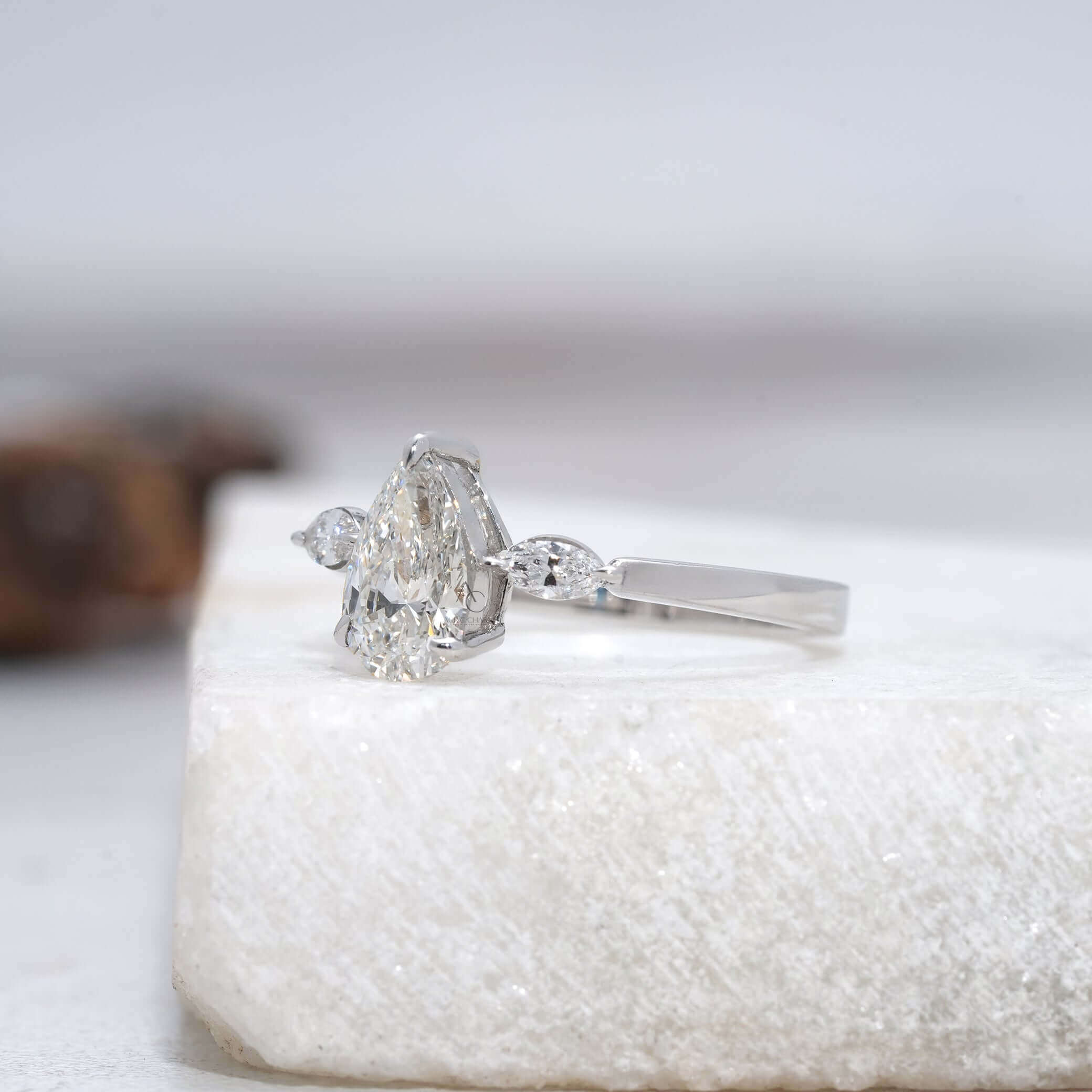 Pear diamond ring with side marquise stones and a sleek metal band.