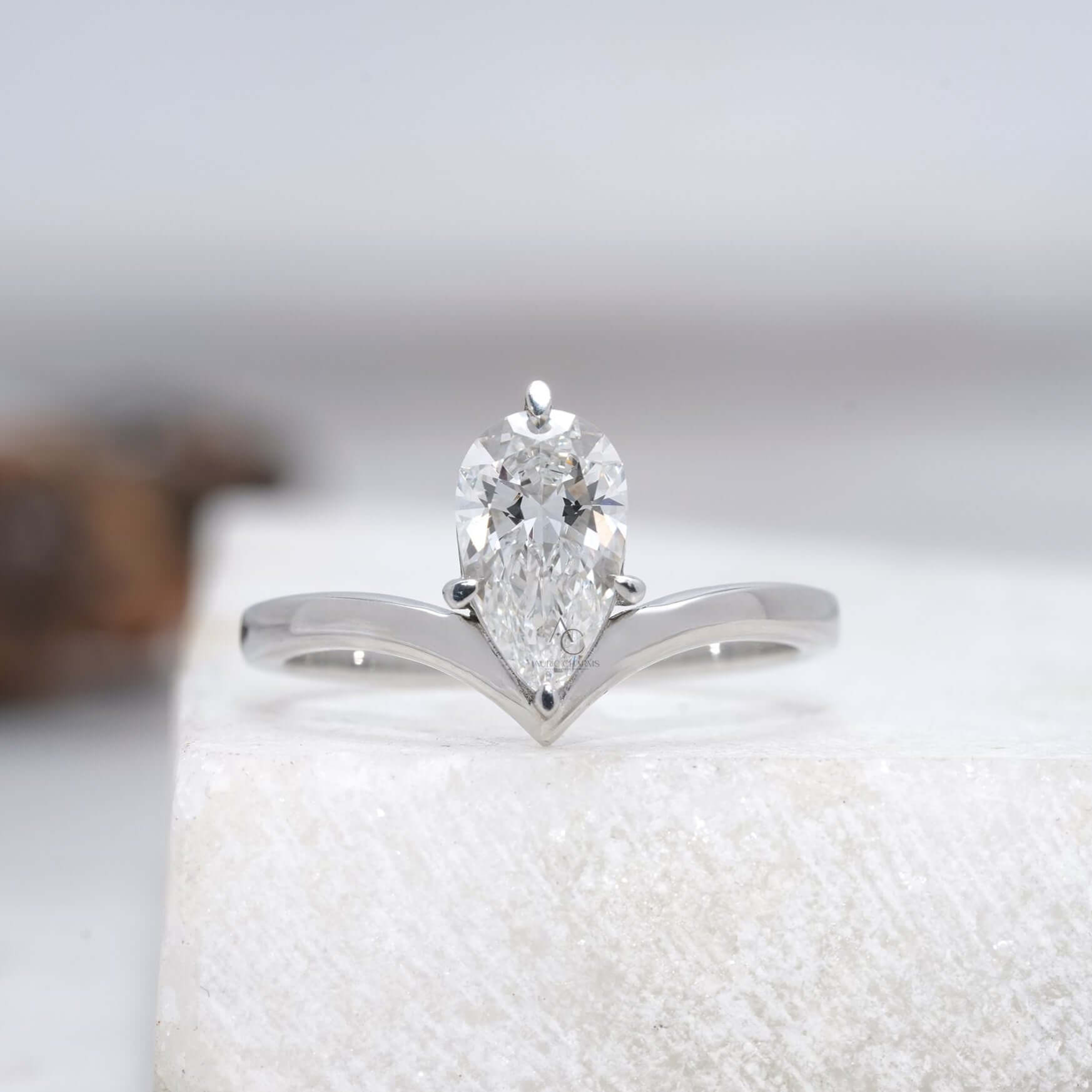 Elegant pear-cut diamond engagement ring with a minimalist V-shaped band, reflecting its brilliance on a glossy surface.