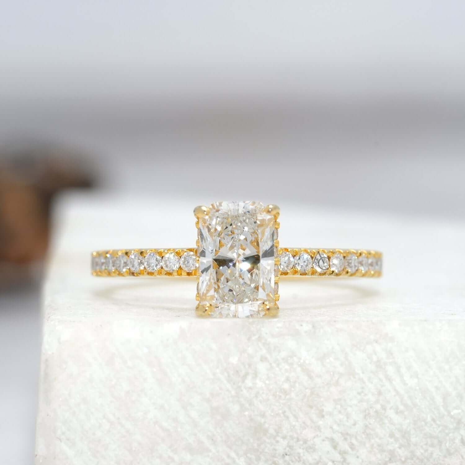 Radiant-cut diamond engagement ring with pavé band reflecting brilliance on a sleek surface.