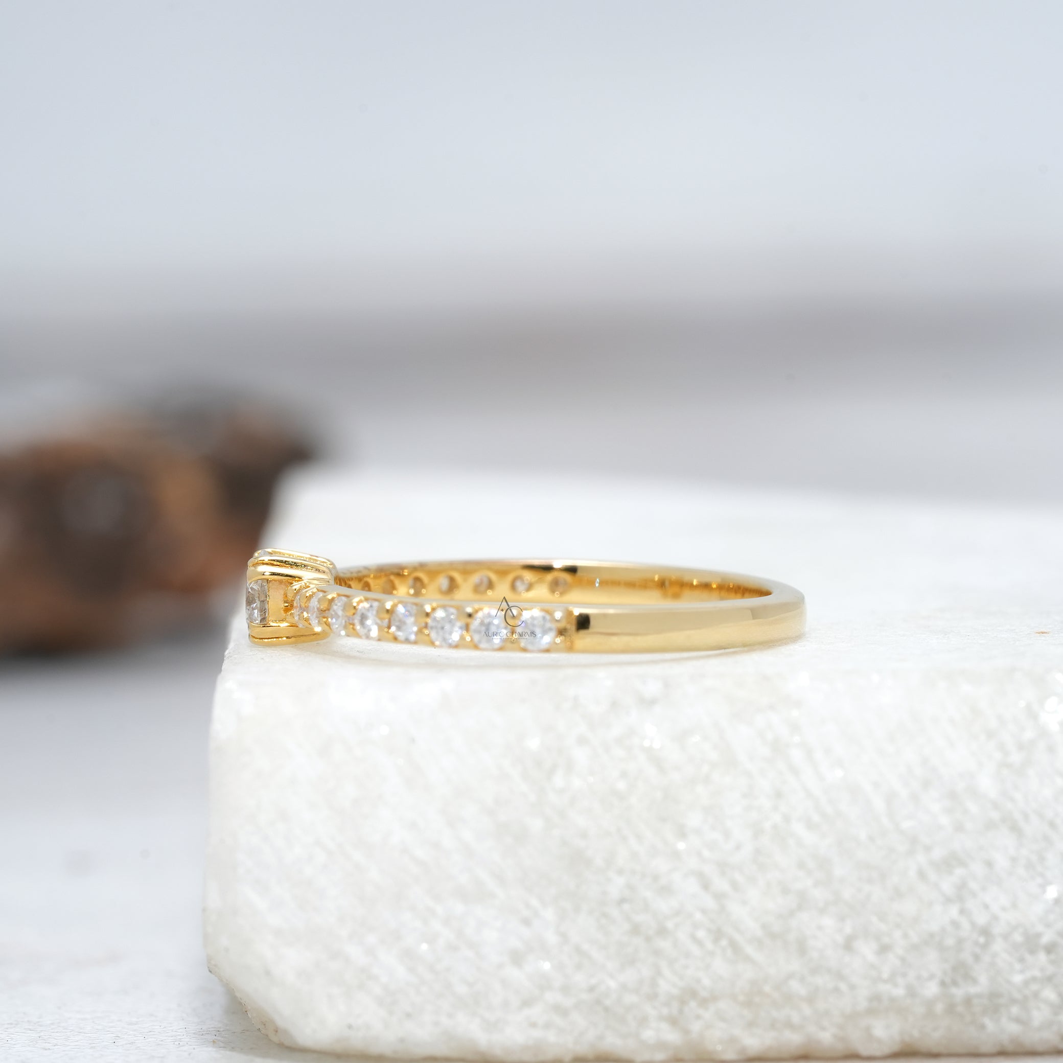 Close-up of a round-cut diamond solitaire ring with a pave band, highlighting its sleek side design and luxurious brilliance.