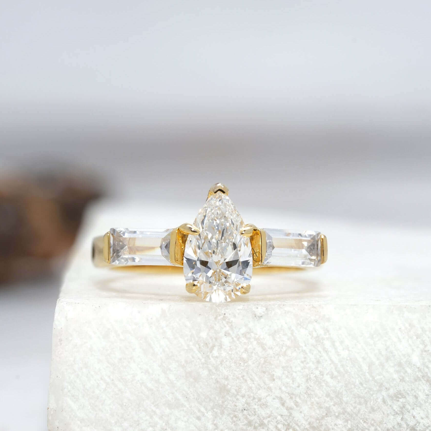 Pear-cut diamond ring with tapered baguette side stones on a reflective surface.