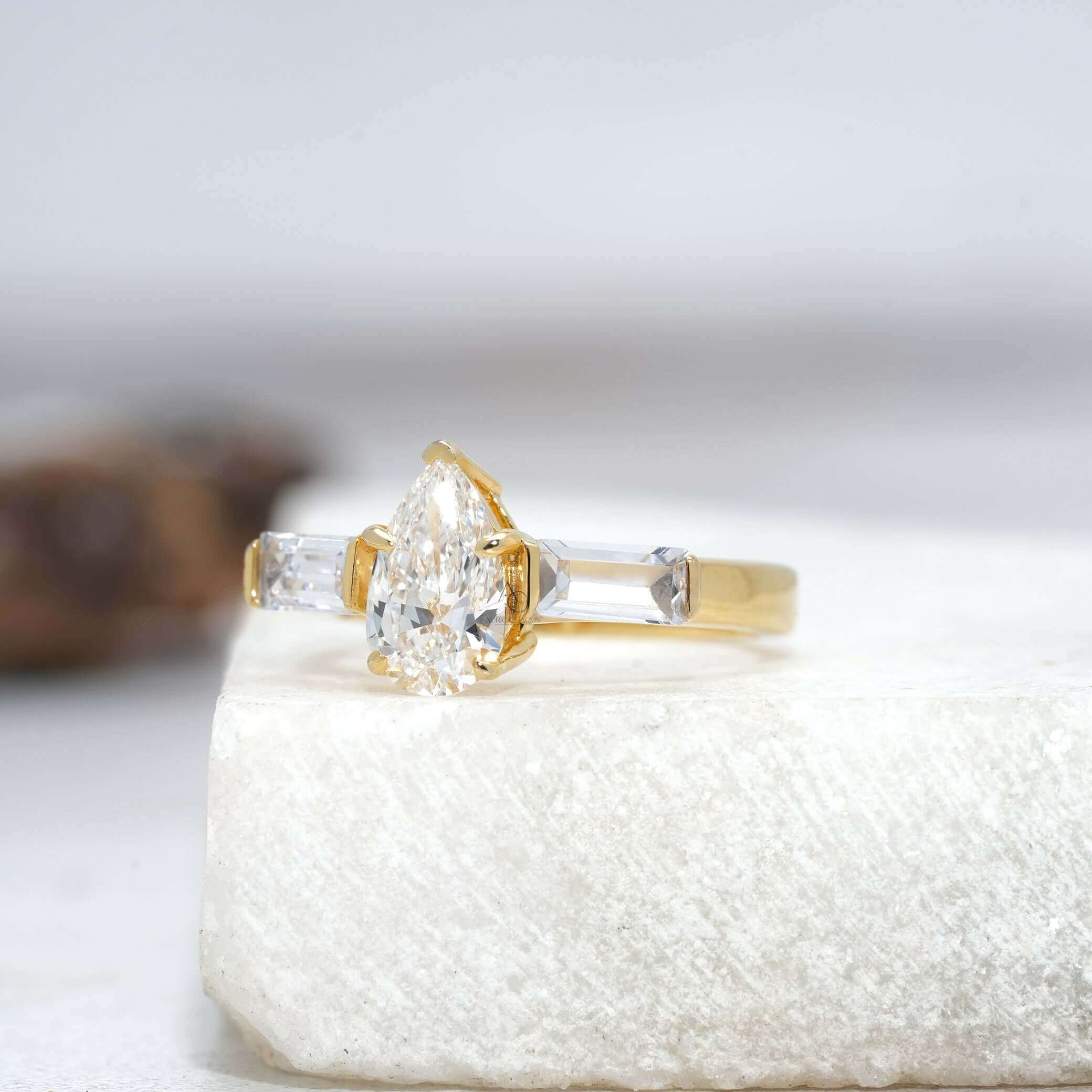 Angled view of a pear-cut diamond ring with intricate side stone and prong setting design.