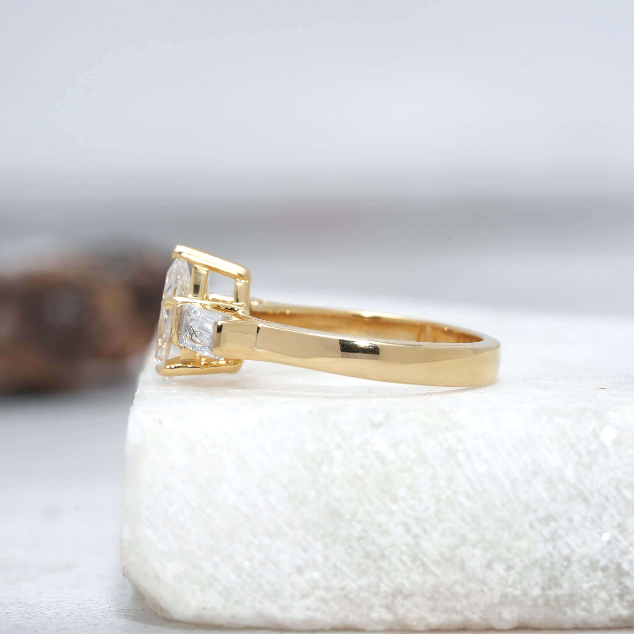 Side view of a pear-cut diamond ring featuring baguette side stones and sleek metal band.