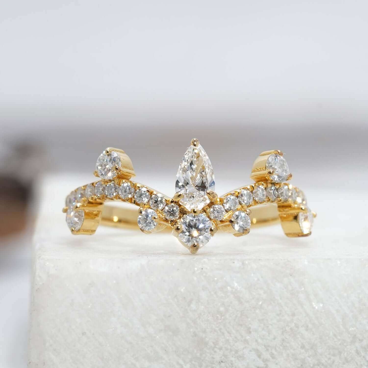 Elegant pear-shaped diamond crown ring with sparkling accent stones on a reflective surface.