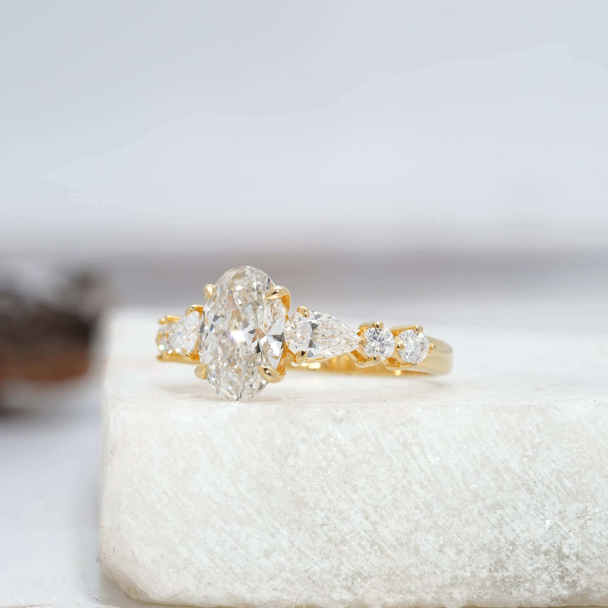 Side view of an oval diamond engagement ring featuring pear-cut and round-cut side stones.