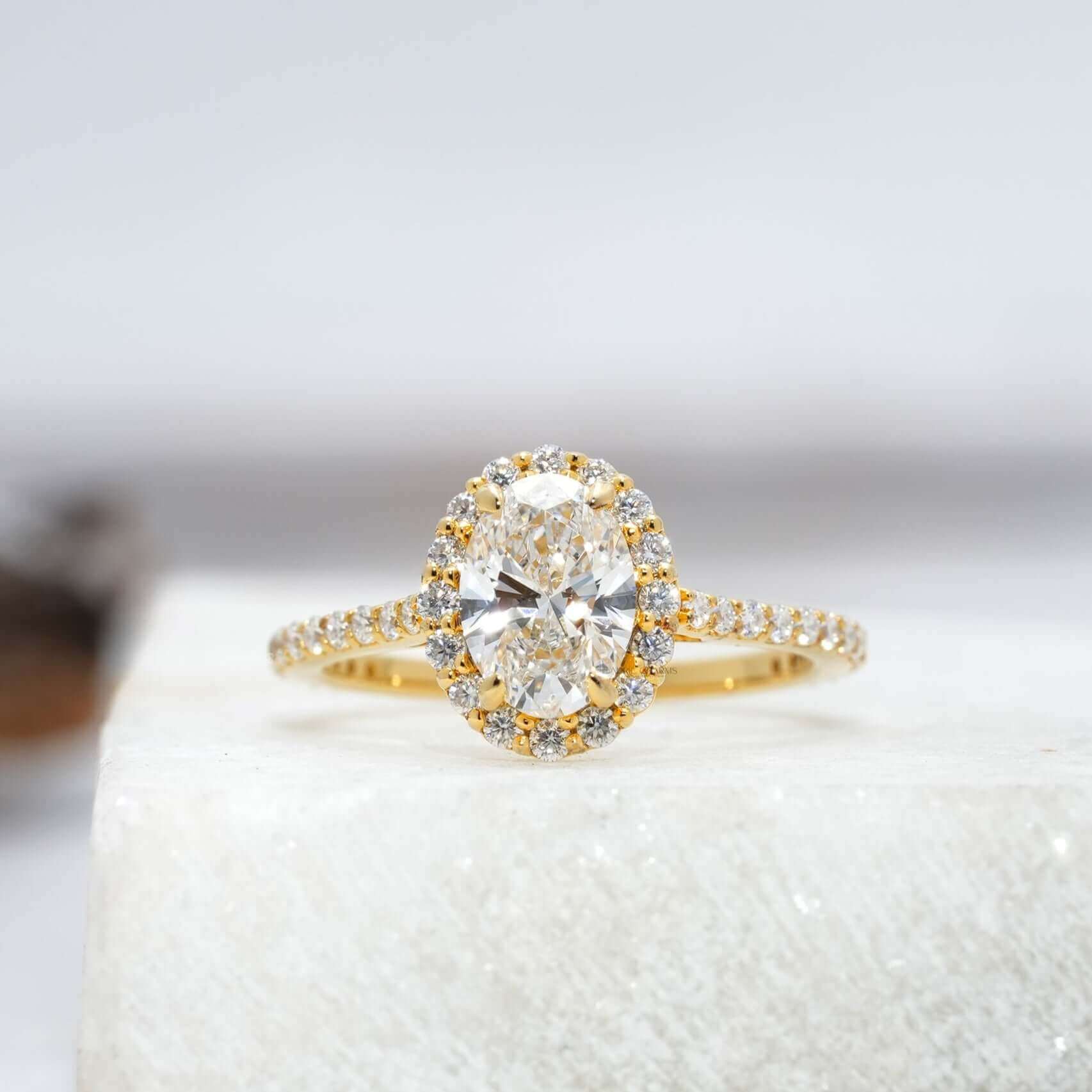 Oval-cut diamond ring with a halo setting and diamond-studded band on a reflective surface.
