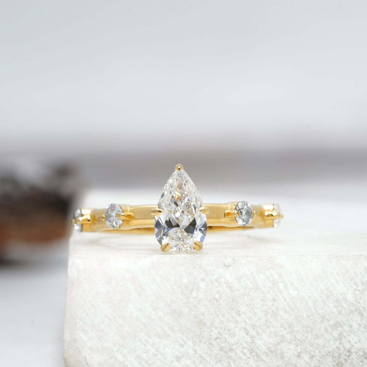 Pear-cut diamond engagement ring with unique detailing on a sleek band, featuring lab-grown diamonds for sustainable elegance.