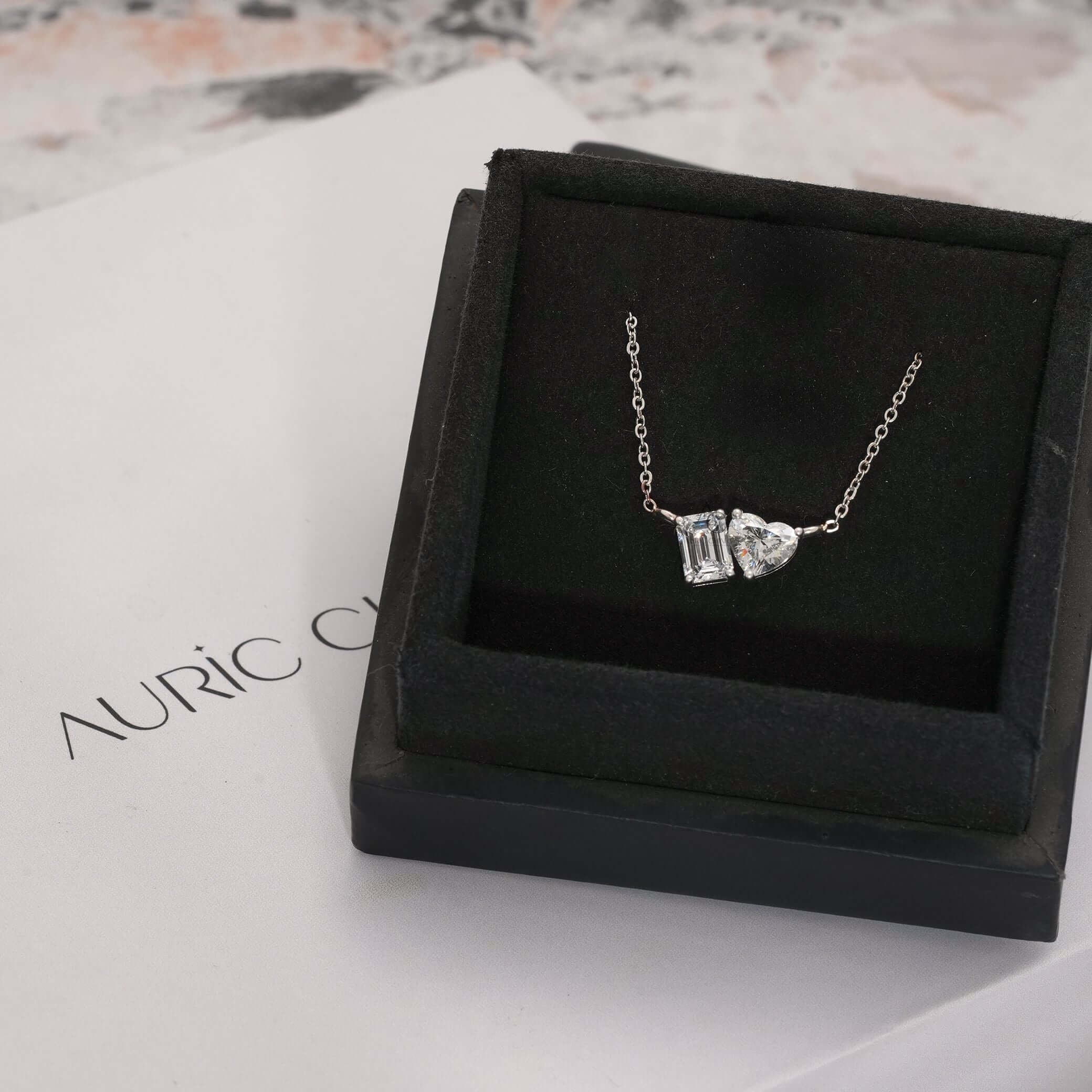 Elegant Toi et Moi pendant with lab-grown Emerald and Heart Cut diamonds, showcased inside a luxury jewelry box.