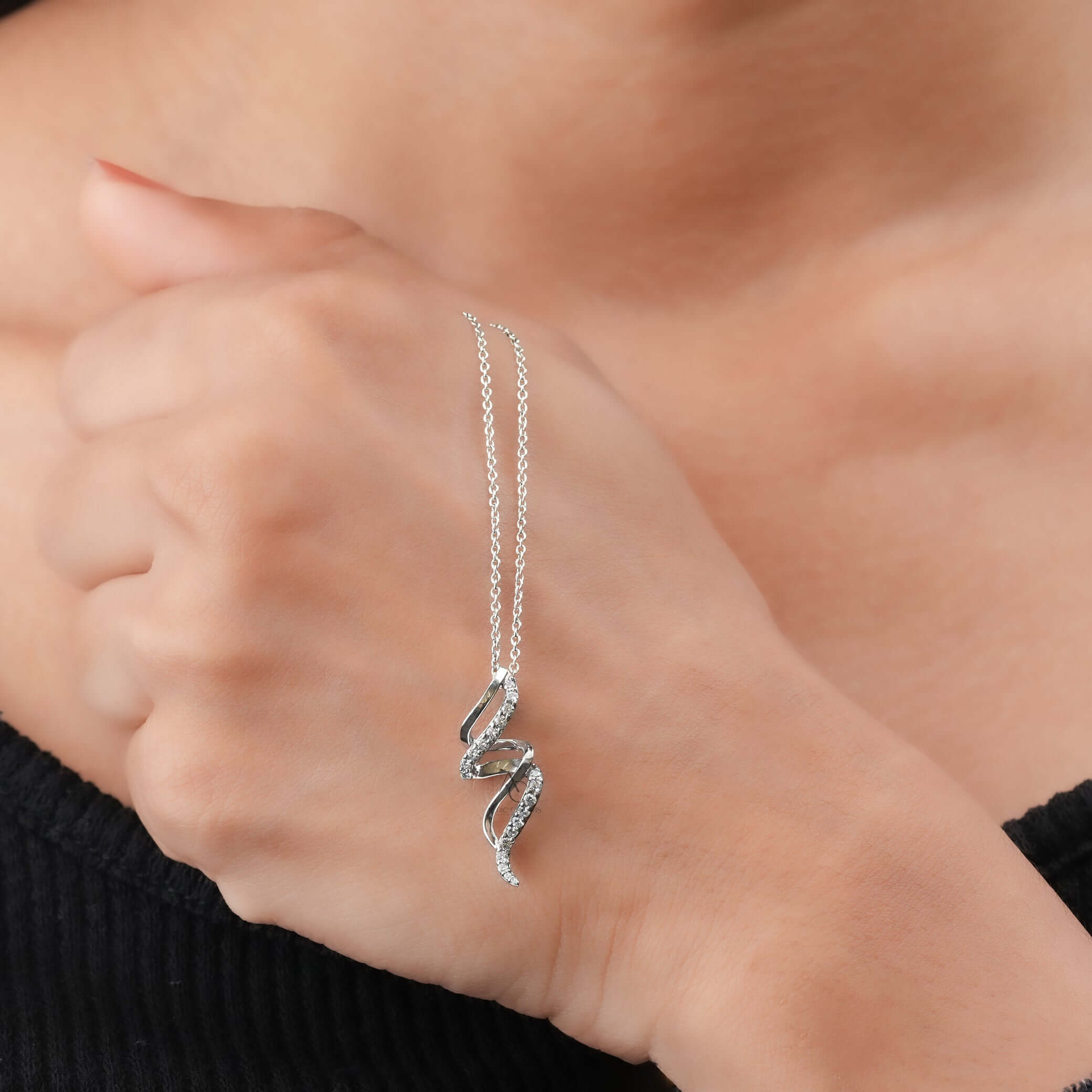 A luxurious curved spiral diamond pendant, shown worn on the hand, highlighting sustainable lab-grown diamonds in fine jewelry.
