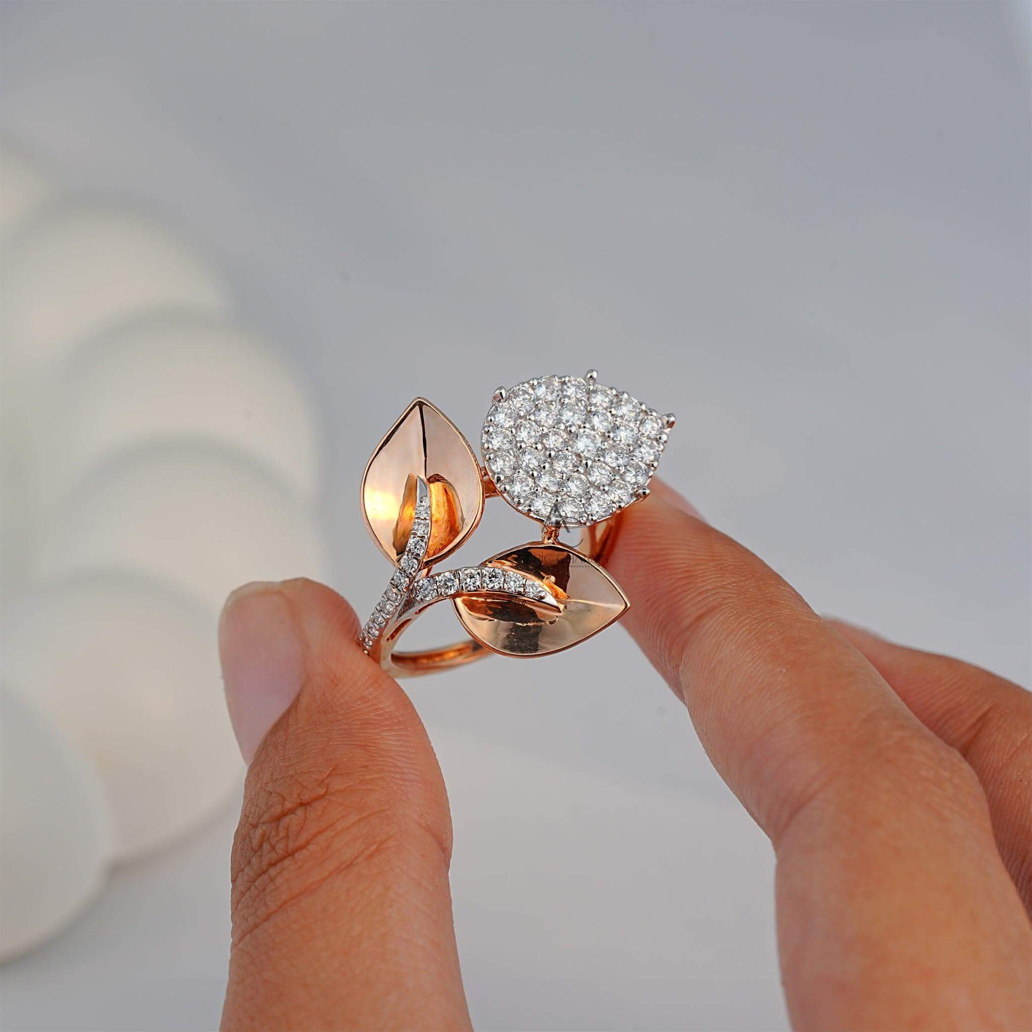 A hand holding a delicate leaf motif ring with a pear-shaped diamond cluster and polished rose gold leaves, illustrating its intricate craftsmanship.