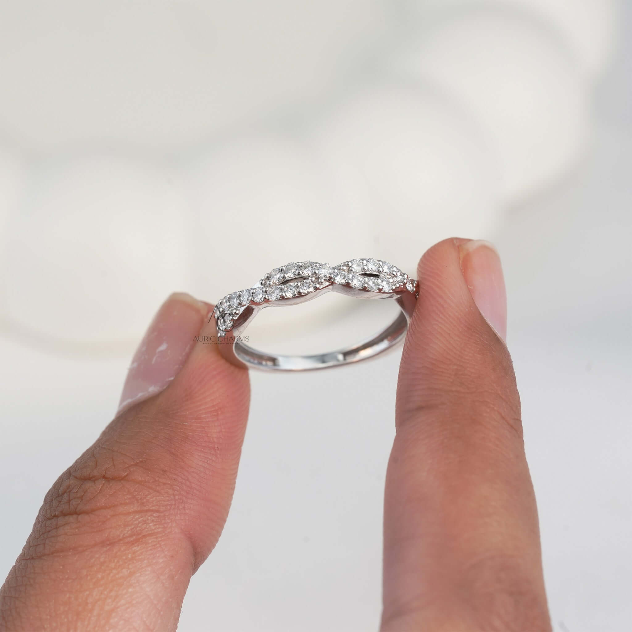 Close-up of diamond ring with intricate design held between fingers.