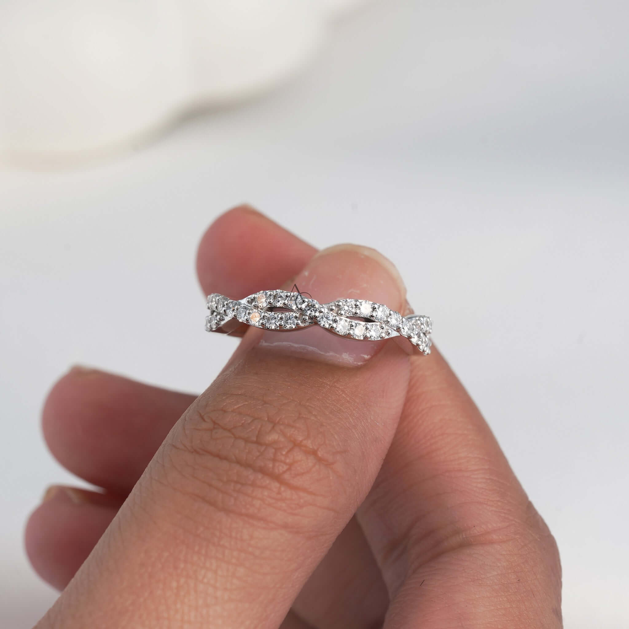 Hand holding diamond ring with twisted band design.