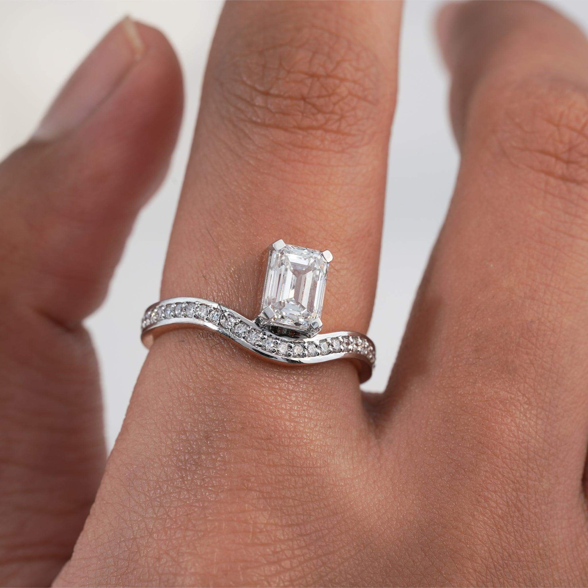 Emerald-cut diamond ring with a delicate curved band on a hand.