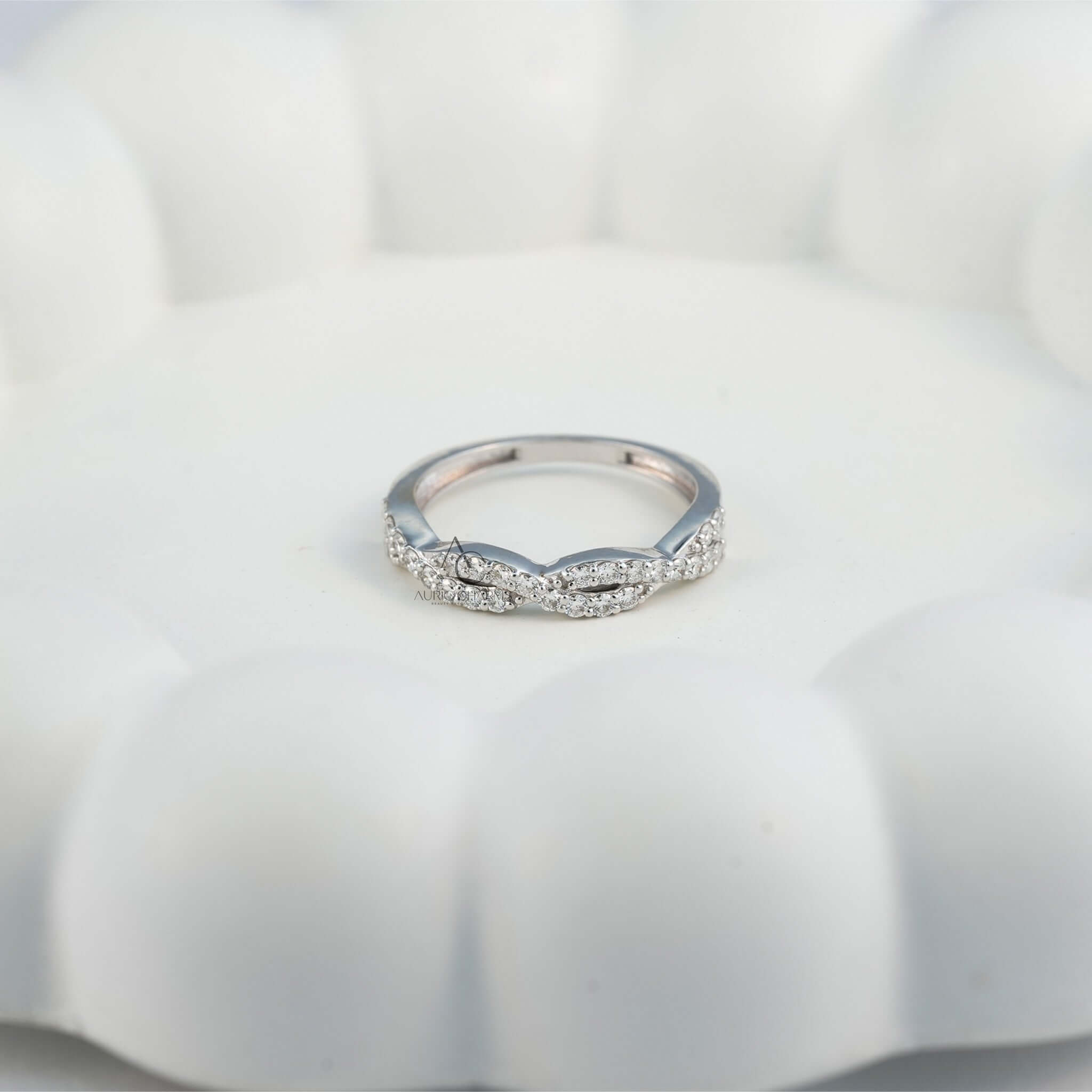 Diamond ring with twisted band resting on white surface.