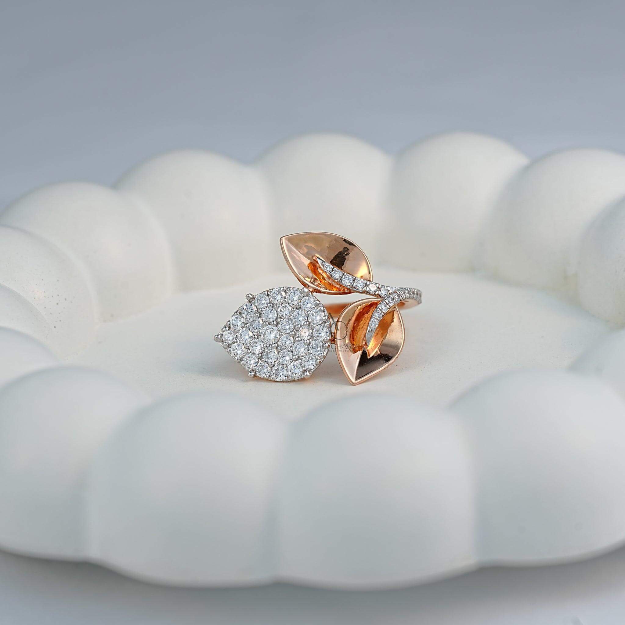 Top view of a nature-inspired diamond ring with rose gold leaves and a sparkling pear-shaped diamond cluster, showcased on a soft white surface