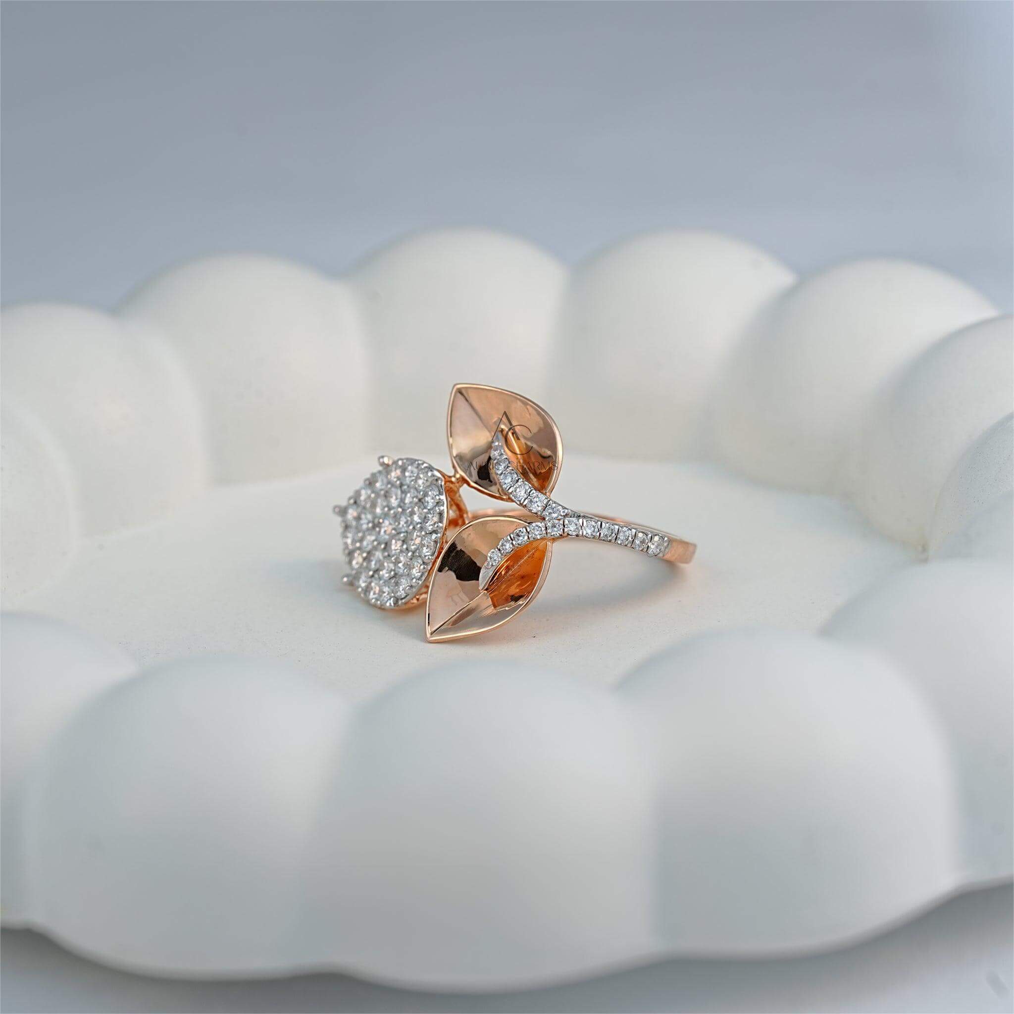 A designer ring displayed on a decorative white surface, highlighting its pear-shaped diamond cluster and rose gold leaf elements with pave diamond accents.