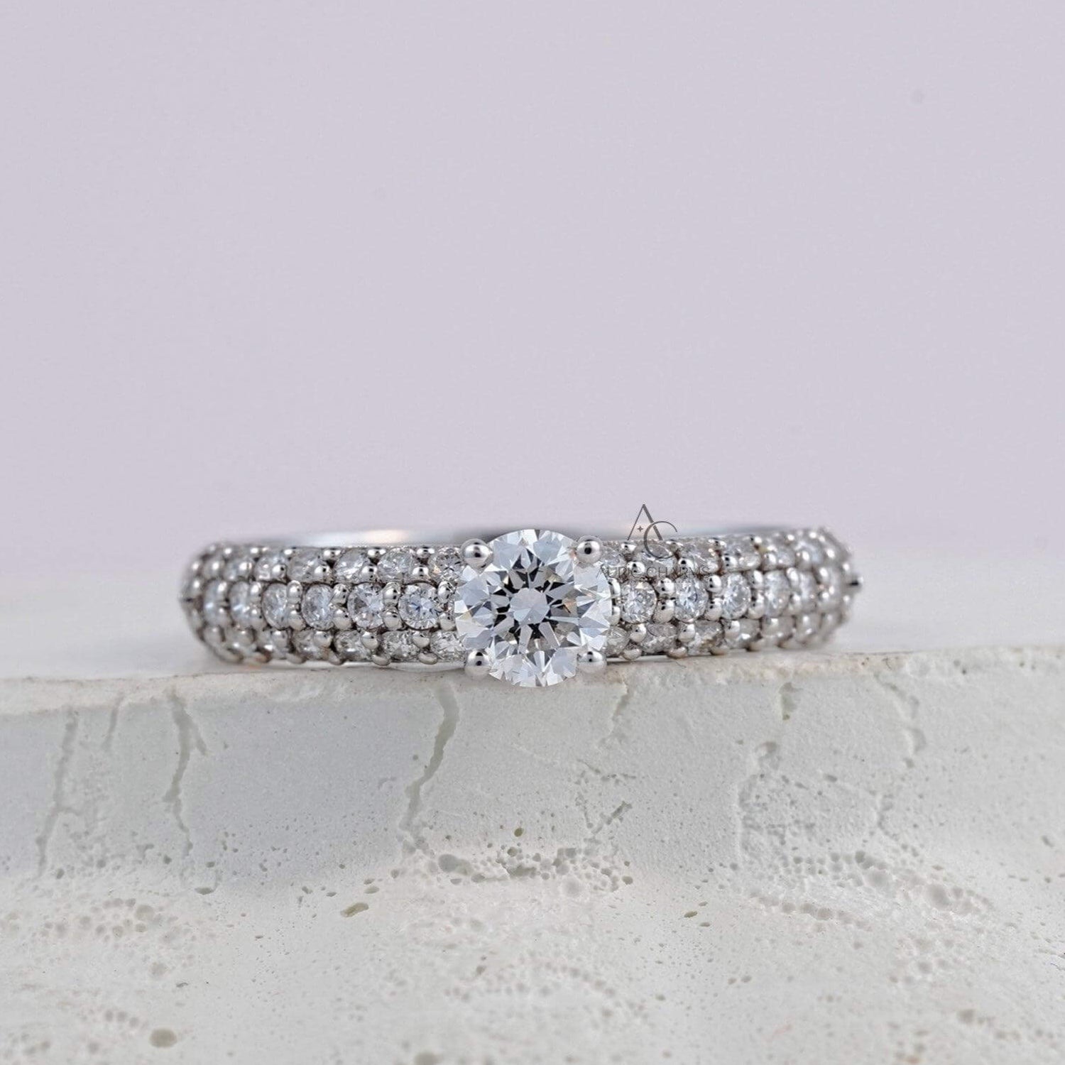 A sparkling diamond ring featuring a round-cut center diamond, set on a platinum band with three rows of pavé diamonds for a luxurious, shimmering effect.