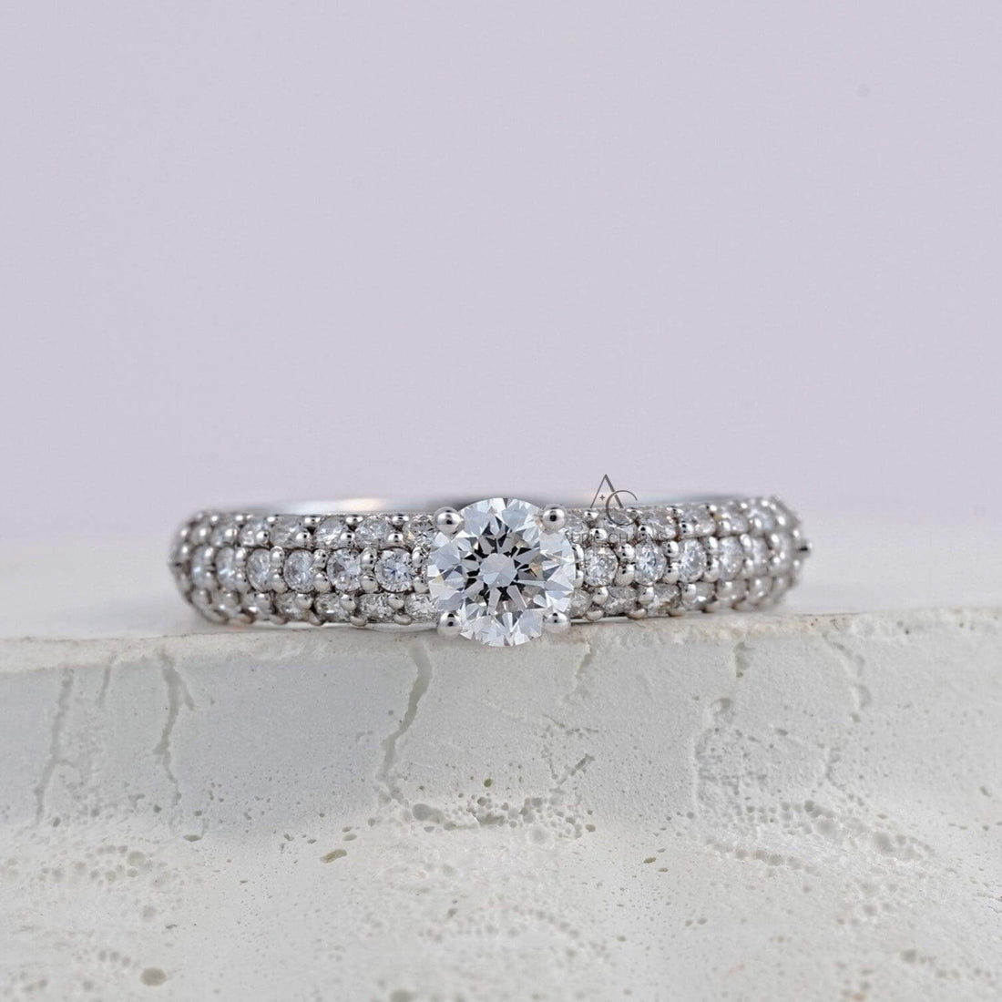 A sparkling diamond ring featuring a round-cut center diamond, set on a platinum band with three rows of pavé diamonds for a luxurious, shimmering effect.