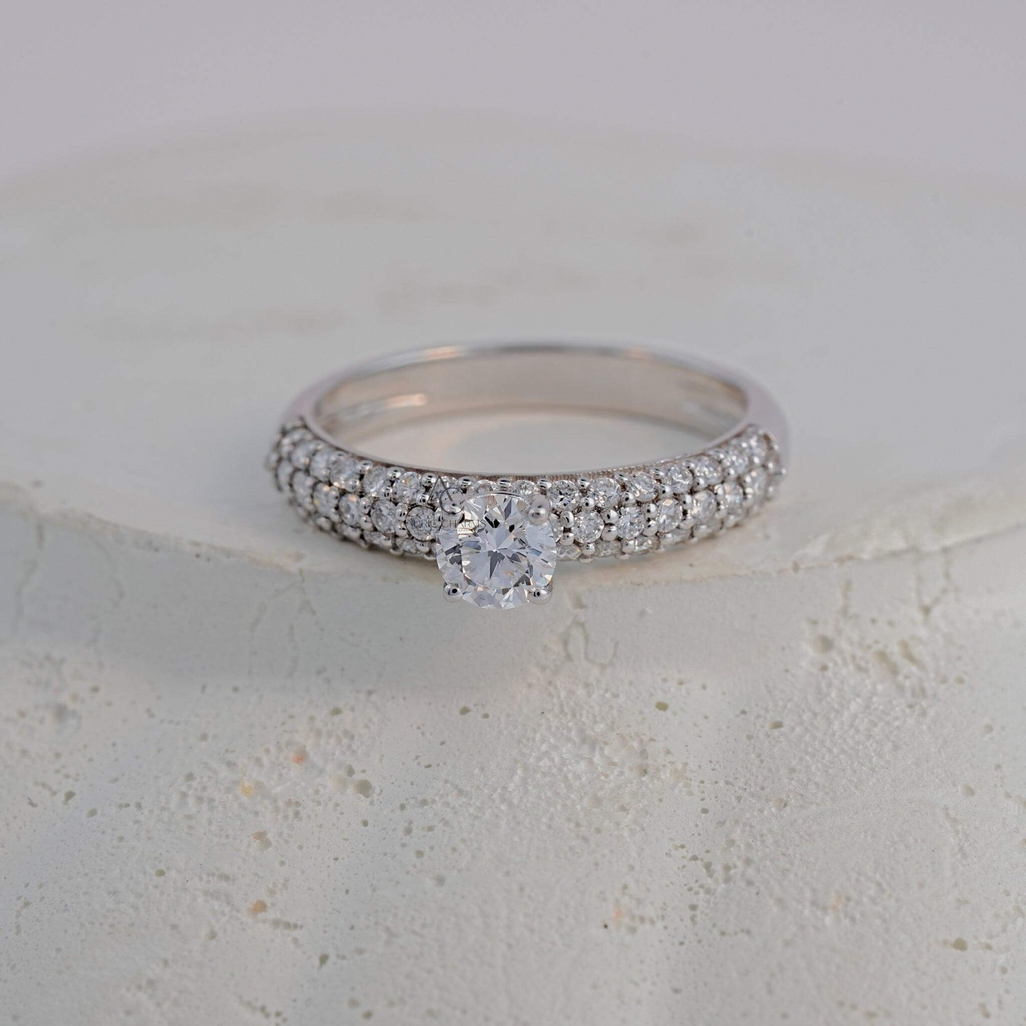 A round-cut diamond solitaire ring with triple rows of pavé diamonds, elegantly presented on a textured white surface.