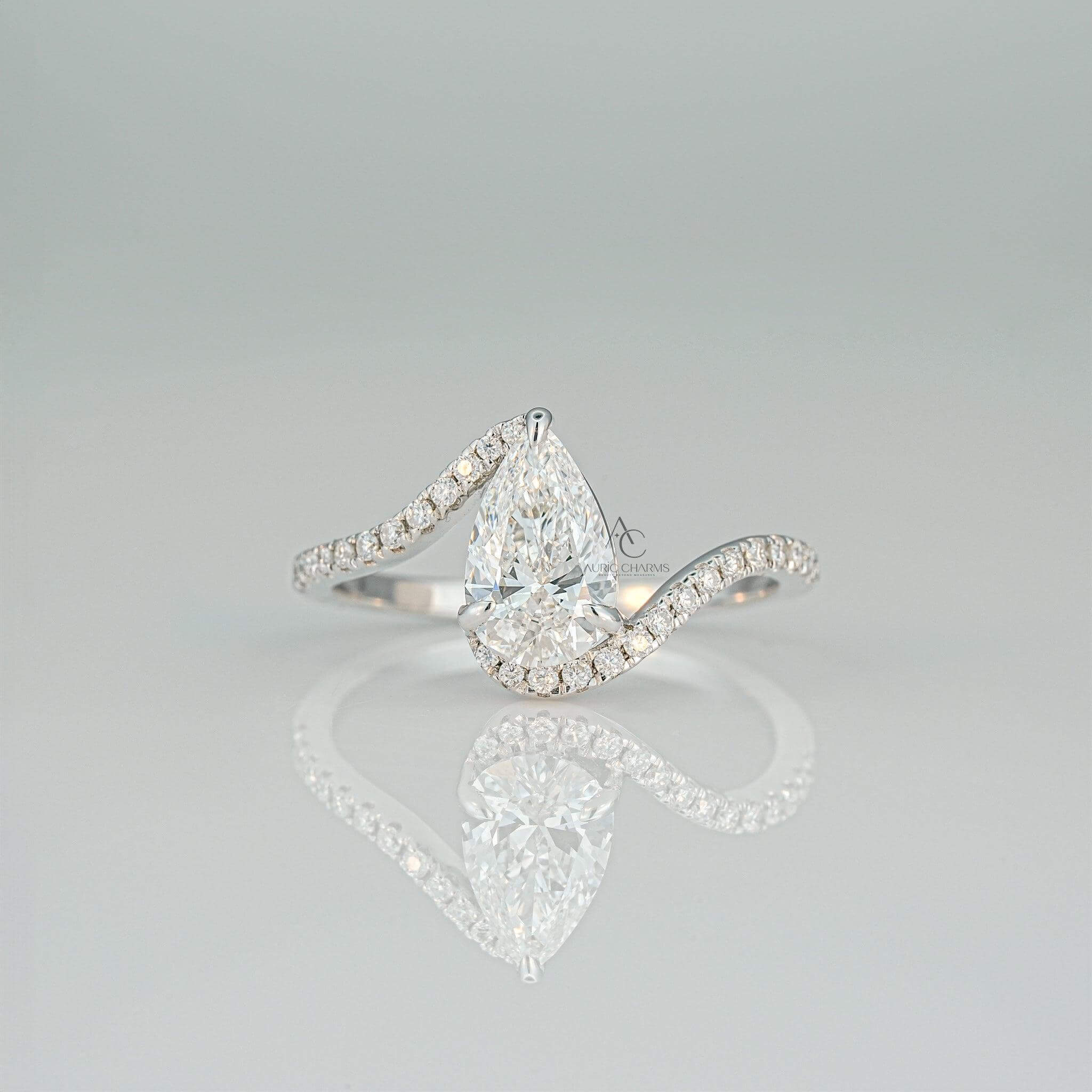Pear-shaped diamond ring with a swirl pavé diamond band on a reflective surface.