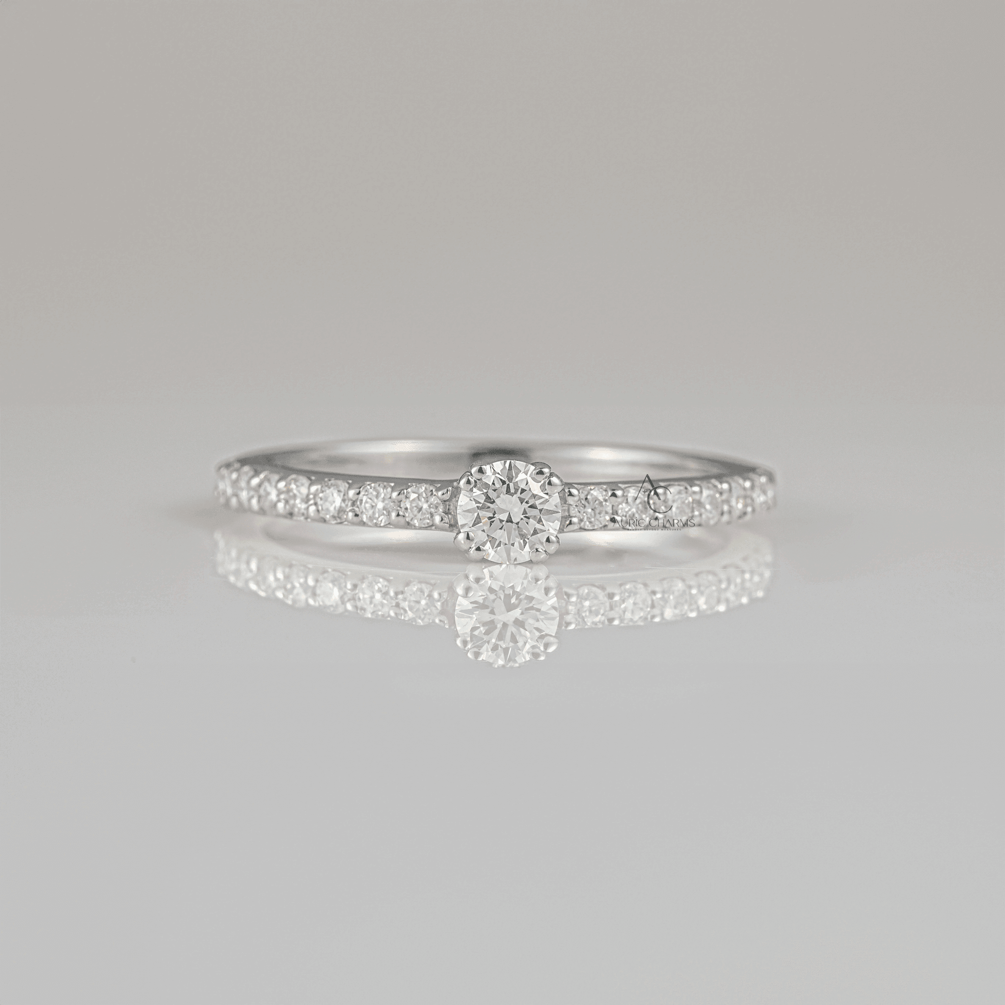 Elegant round-cut diamond solitaire engagement ring with a sparkling pave band displayed on a reflective surface, perfect for engagement proposals.