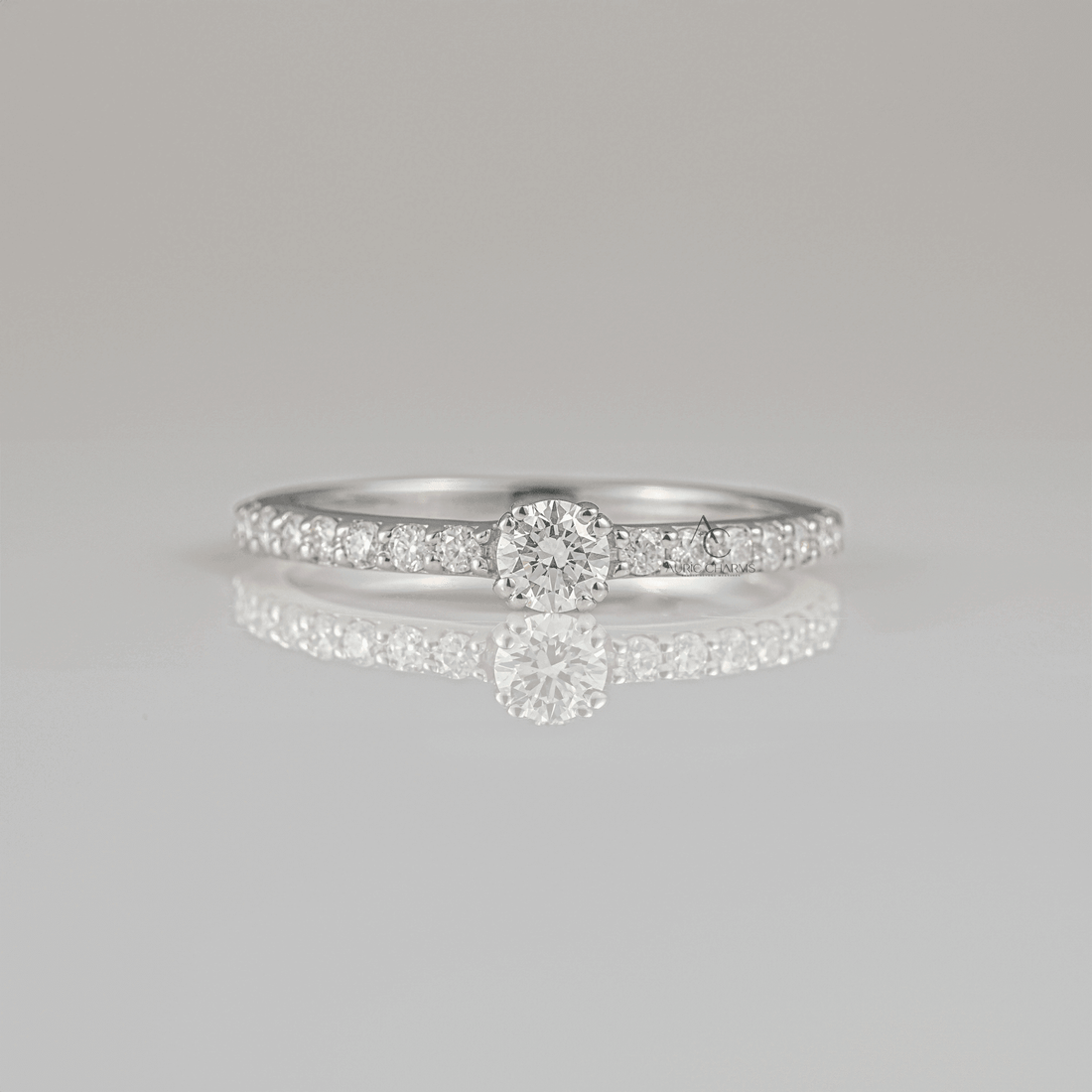 Elegant round-cut diamond solitaire engagement ring with a sparkling pave band displayed on a reflective surface, perfect for engagement proposals.
