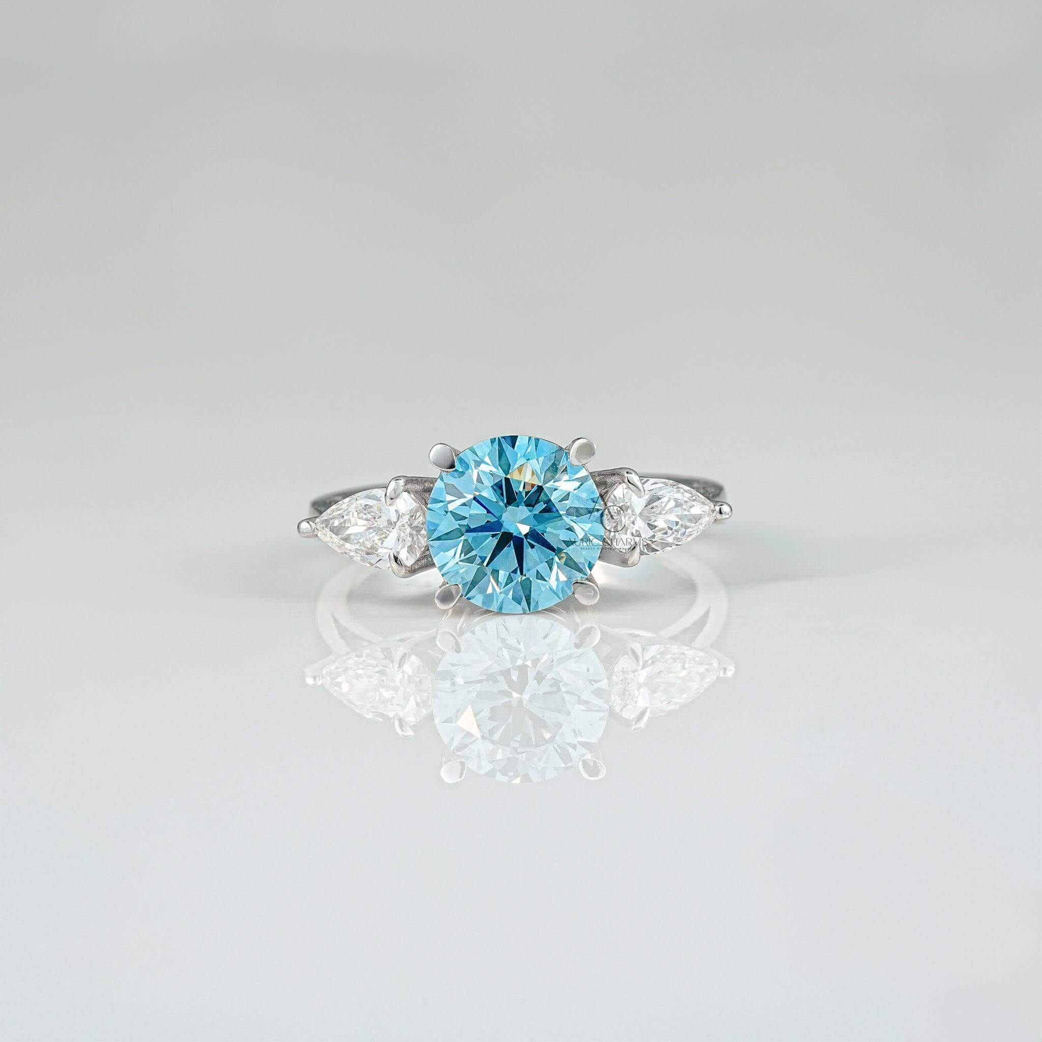 Elegant three-stone ring featuring a vibrant round blue diamond centerpiece with pear-cut side stones.