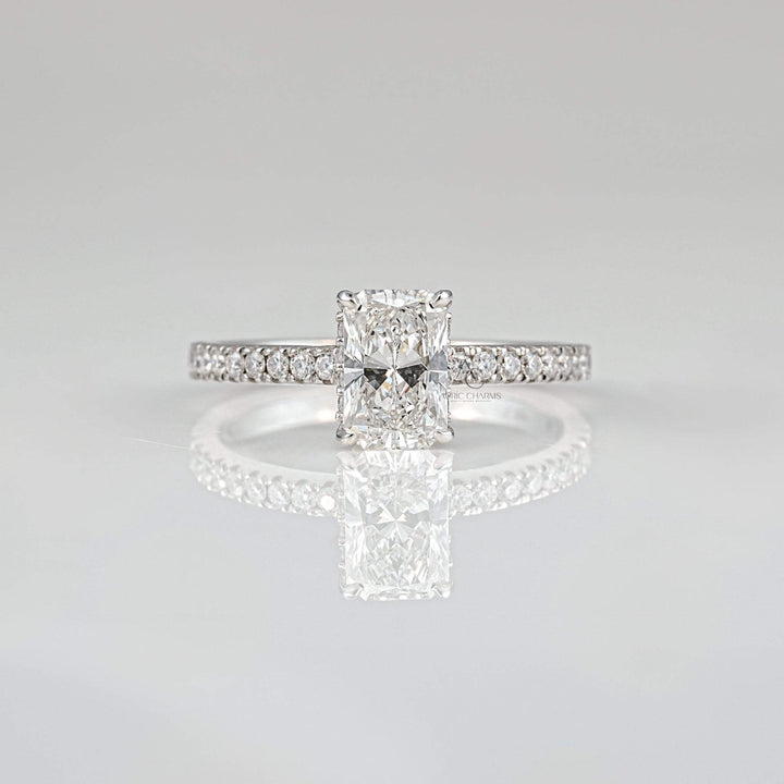 Radiant-cut diamond engagement ring with pavé band reflecting brilliance on a sleek surface.