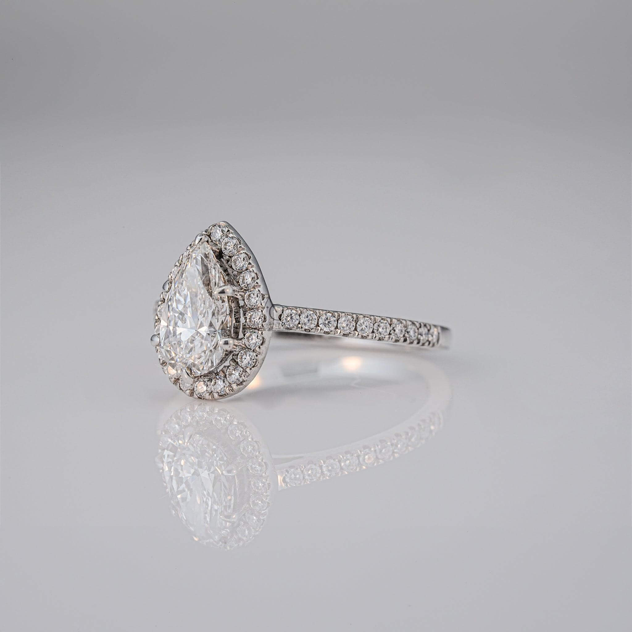 Elegant pear-cut diamond ring with a halo setting on a reflective surface.