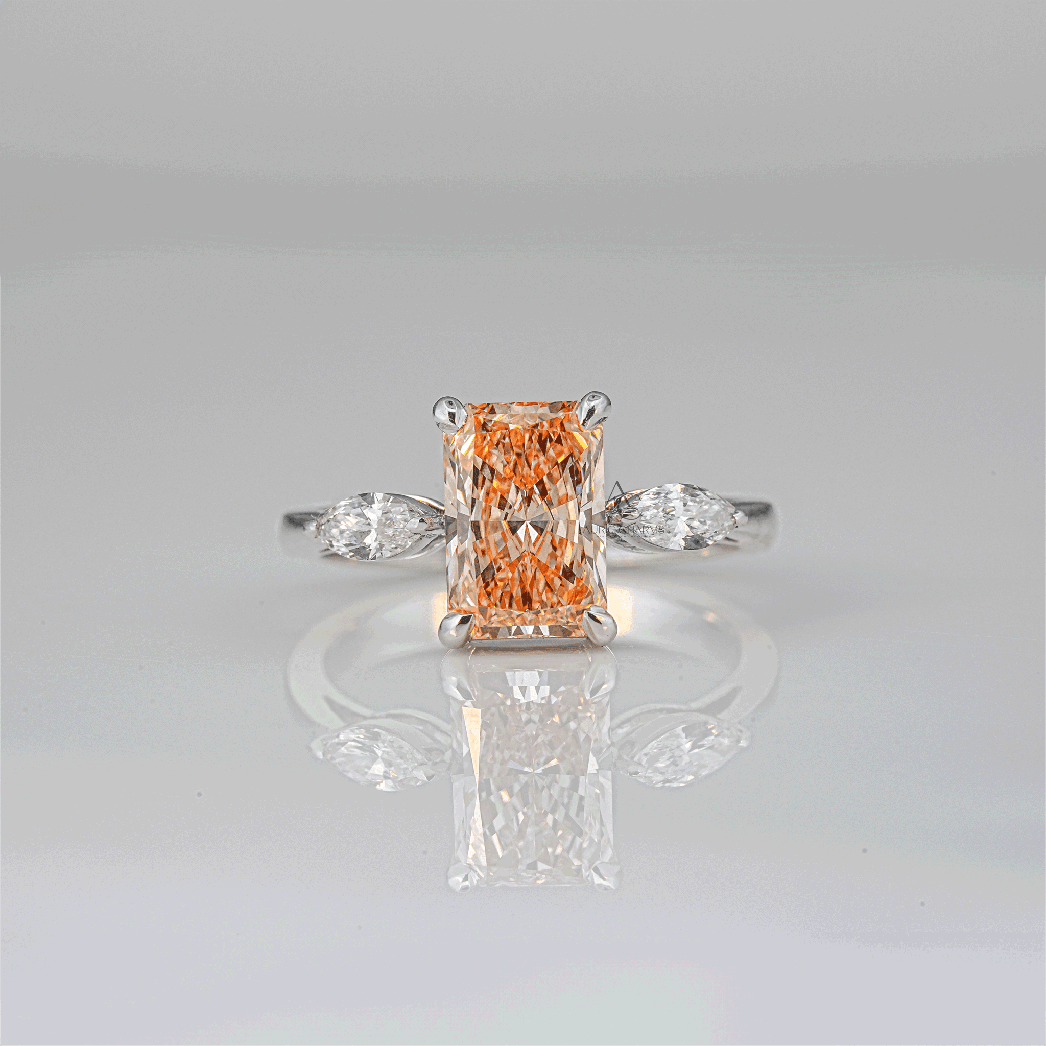 Elegant radiant-cut champagne-colored lab-grown diamond ring on a sleek white gold band with marquise side stones, captured against a reflective surface.
