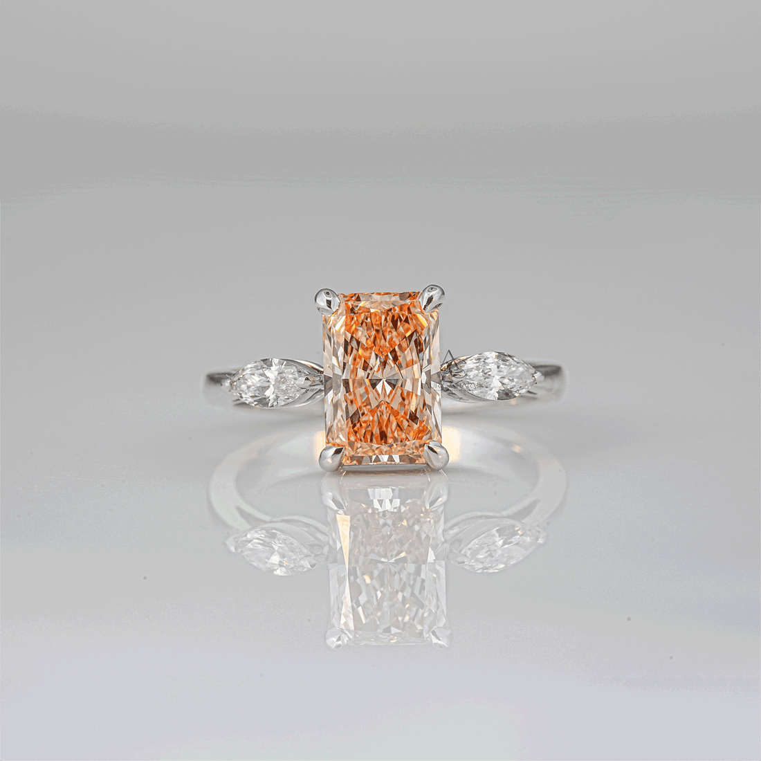 Elegant radiant-cut champagne-colored lab-grown diamond ring on a sleek white gold band with marquise side stones, captured against a reflective surface.