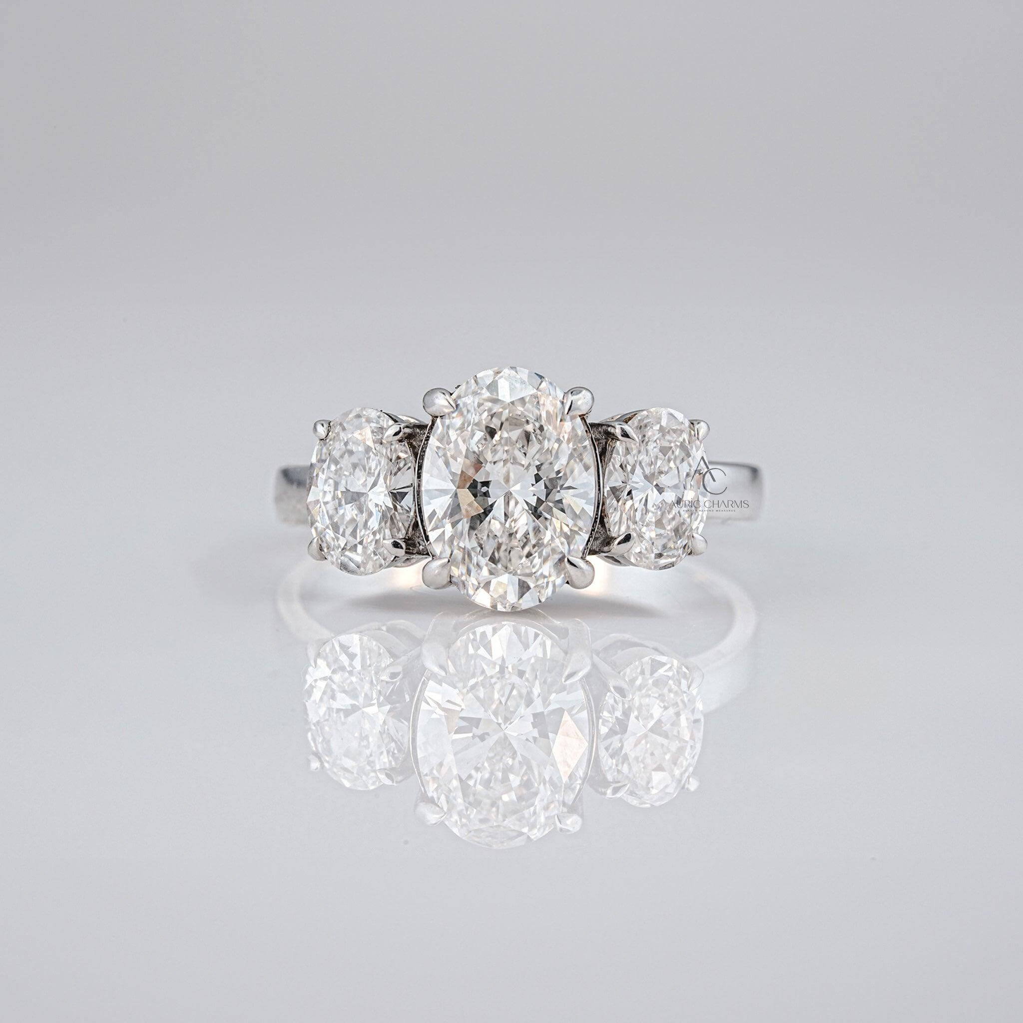 Oval diamond three-stone engagement ring with lab-grown diamonds, set on a reflective surface.