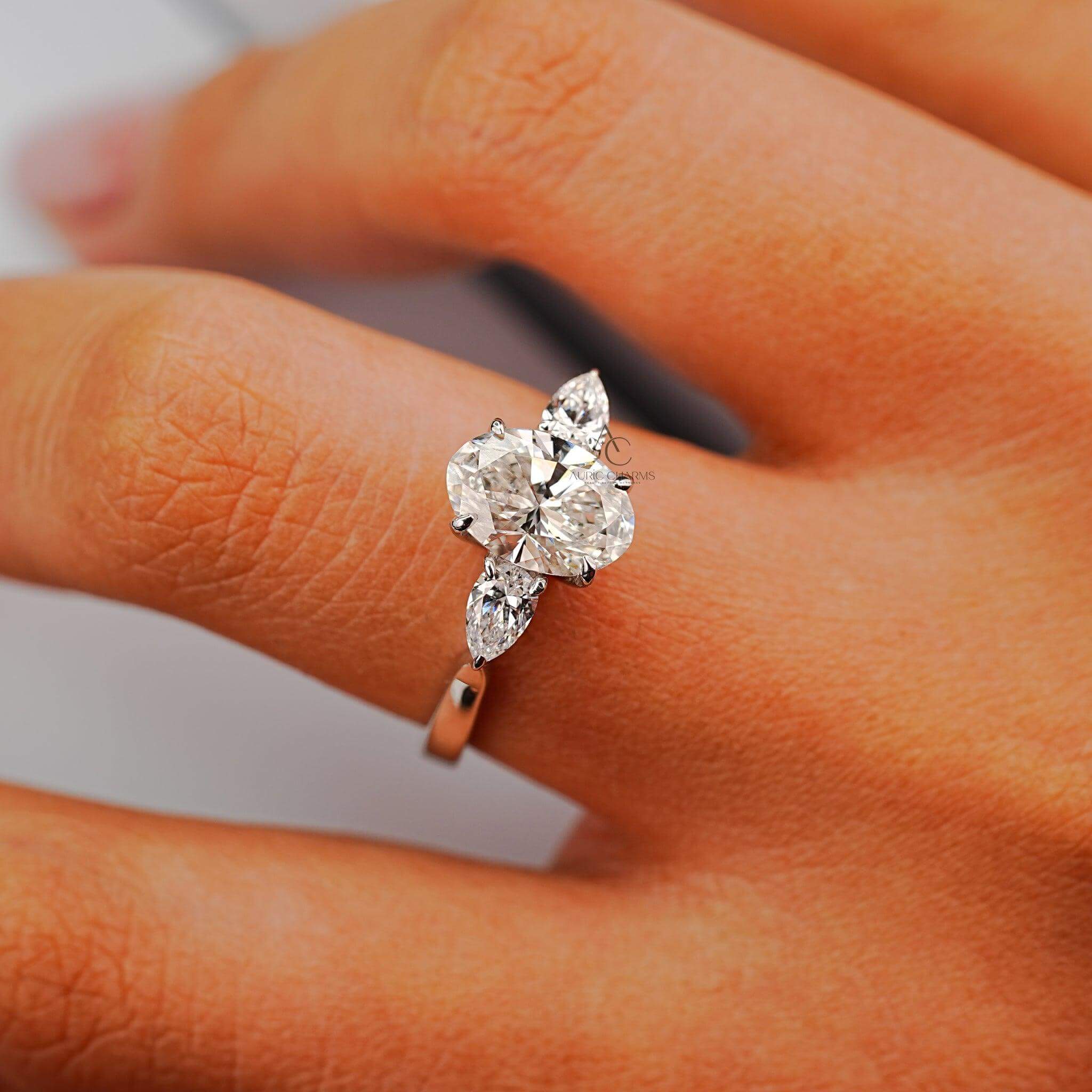 Oval diamond engagement ring with pear-shaped side stones showcased on hand.