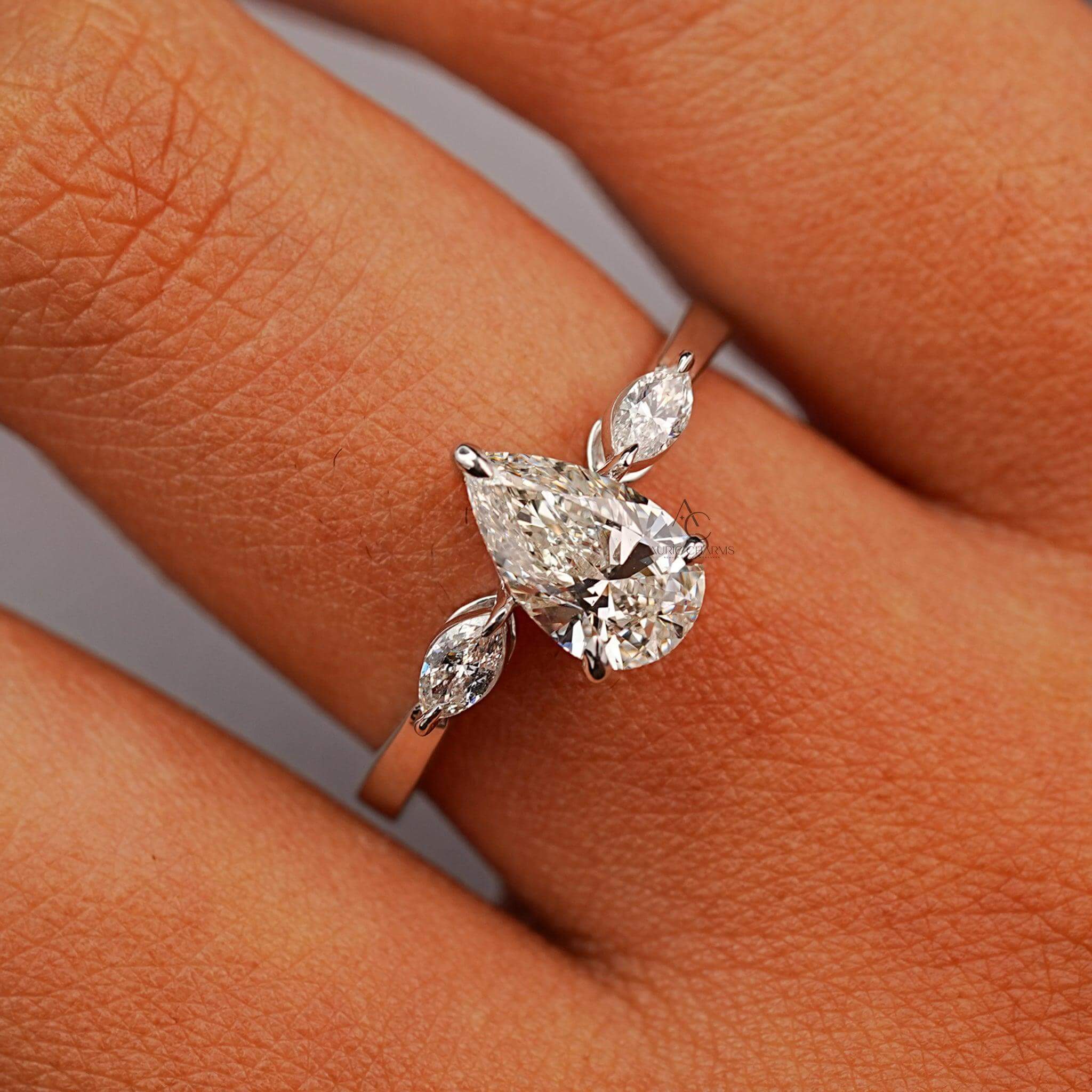 Pear diamond ring with marquise accents shown on a hand for size reference.