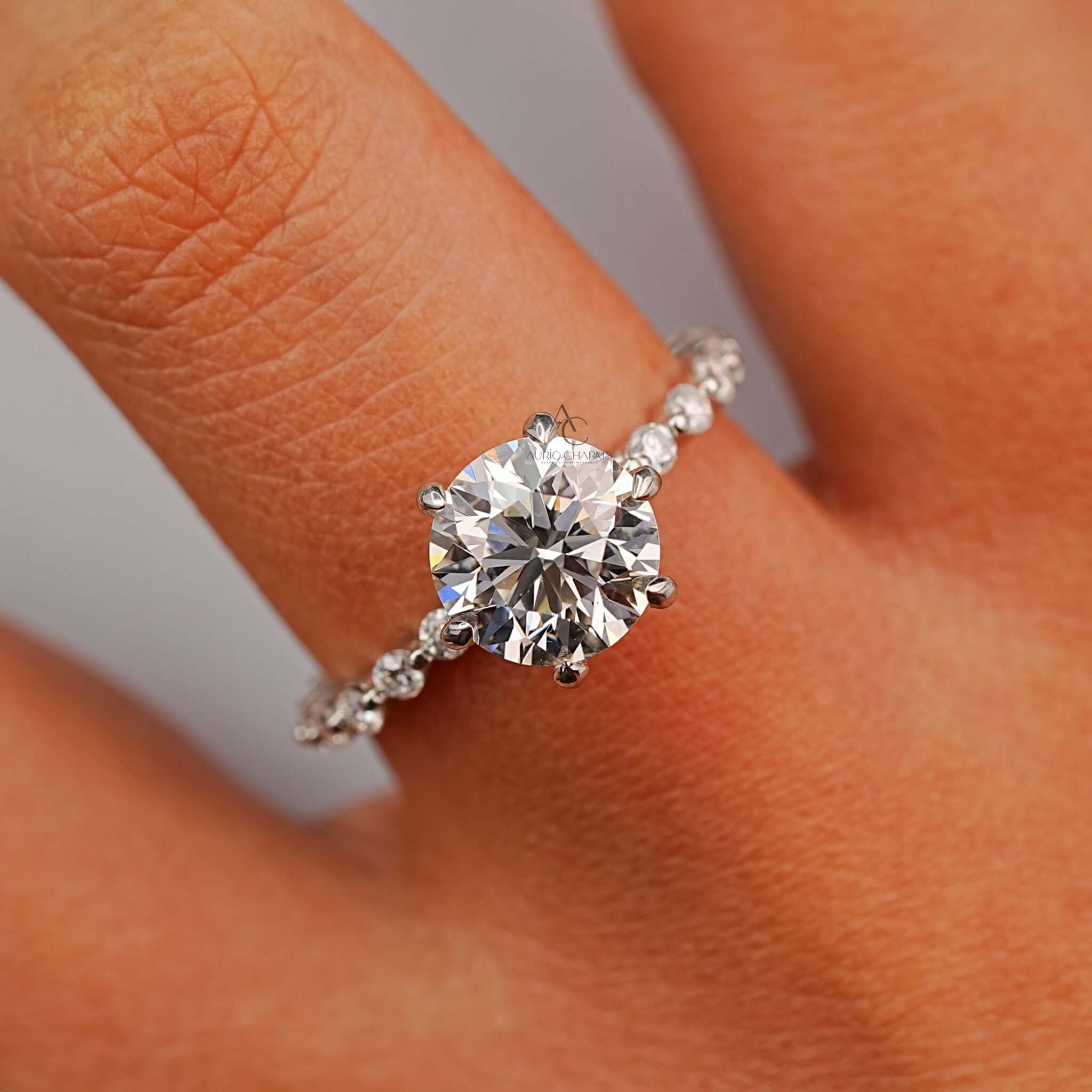 Round-cut diamond ring with pave band, worn on hand showcasing sparkle.