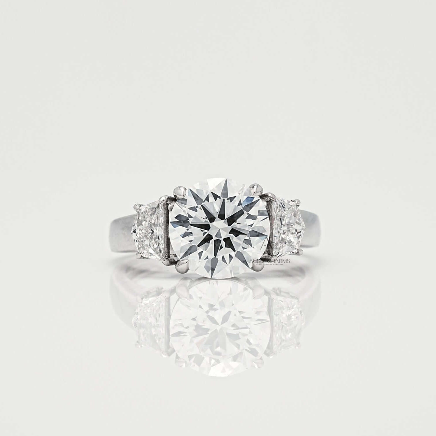 Round brilliant diamond ring with side stones on a reflective surface.