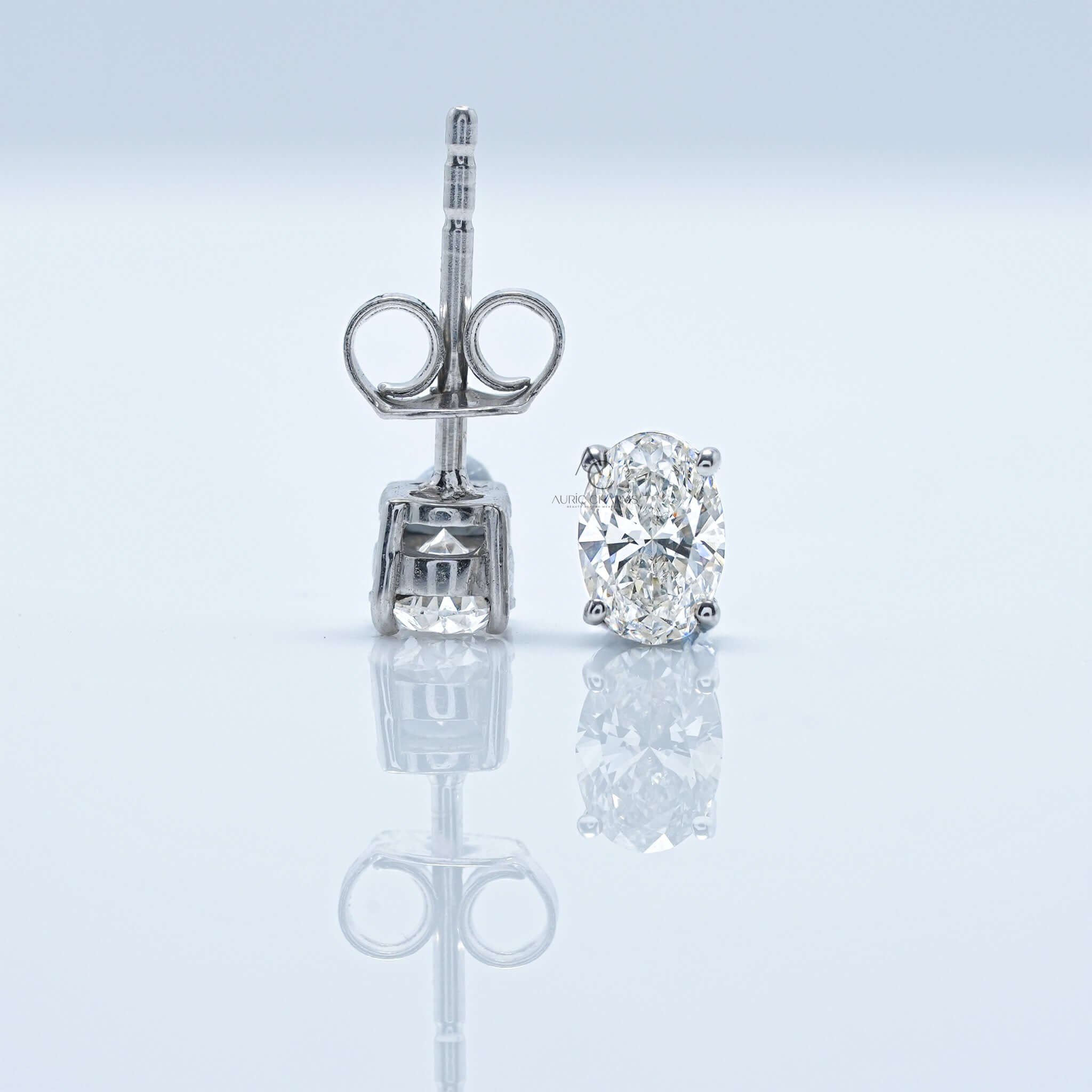 Oval diamond earring upright with post and back, other lays flat.
