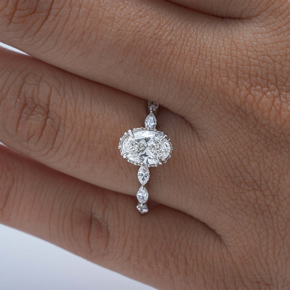 Oval diamond ring worn on finger with marquise side stones.
