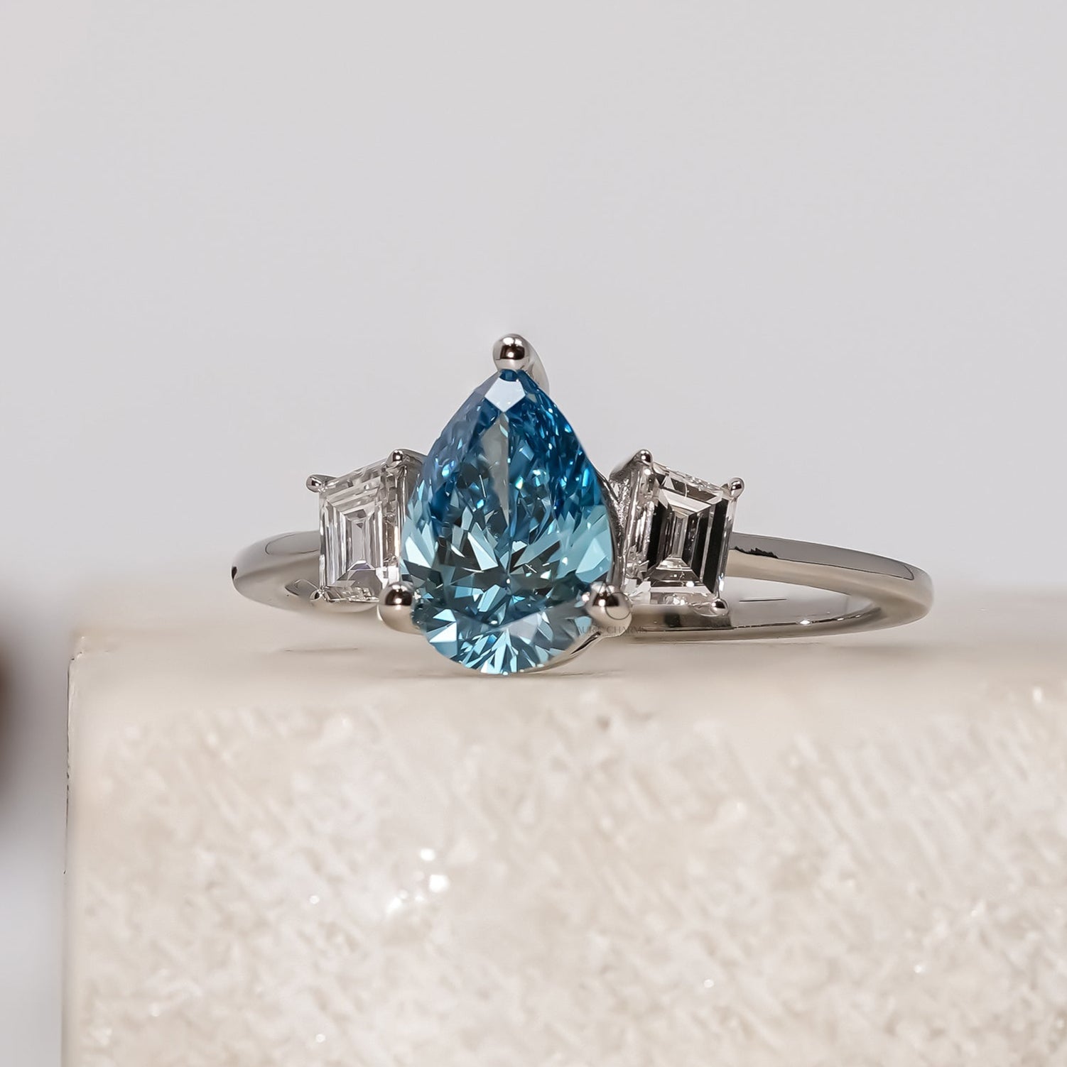 Silver ring with a pear-shaped blue gemstone on a textured white surface