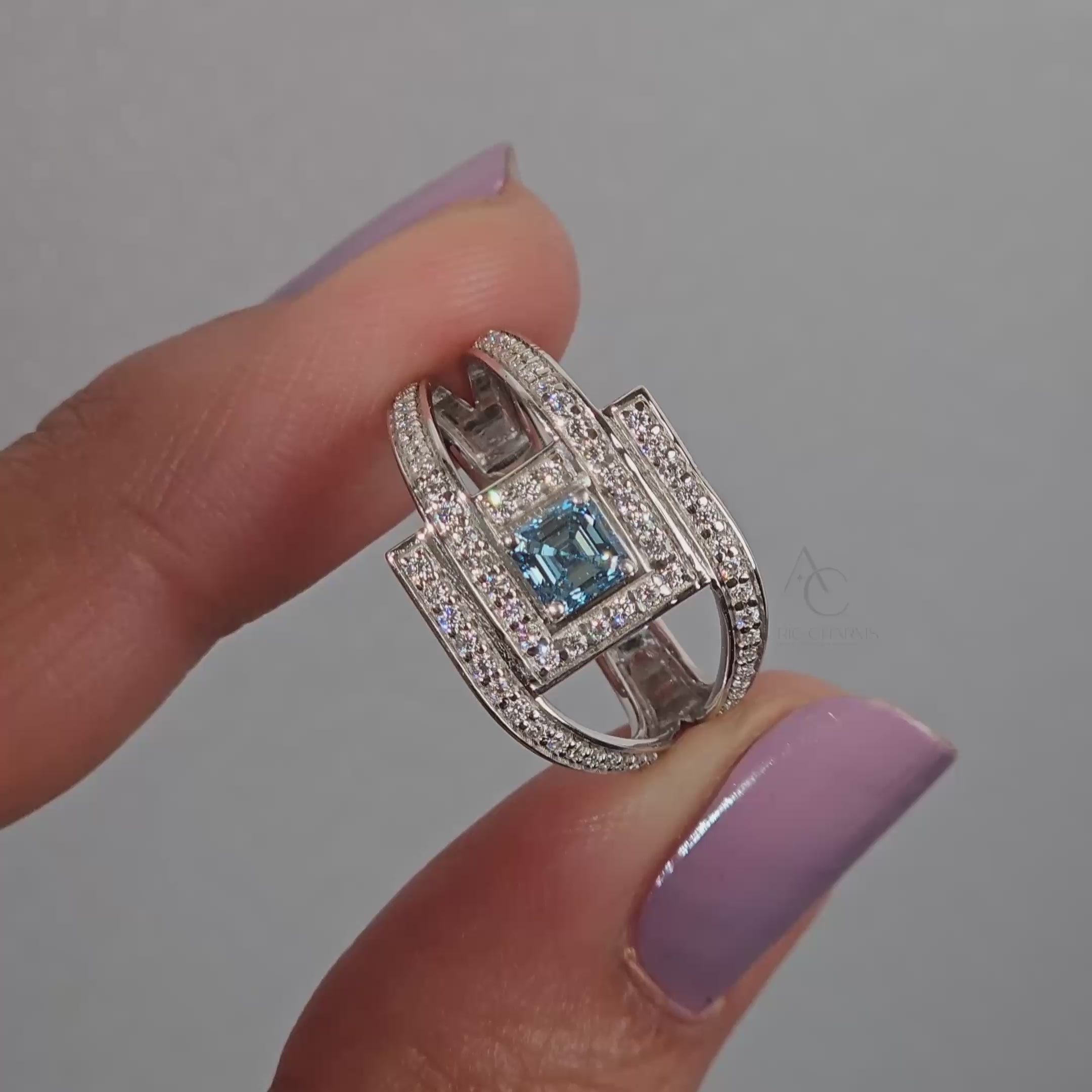 Square blue gemstone ring on finger, featuring diamond accents and modern design.