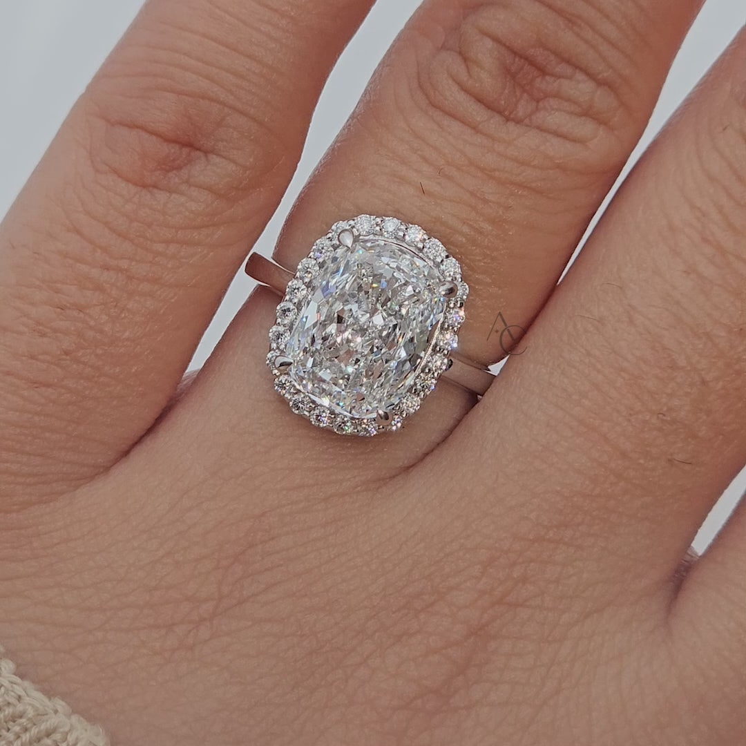 Close-up rotating video of cushion-cut diamond halo ring on reflective surface.