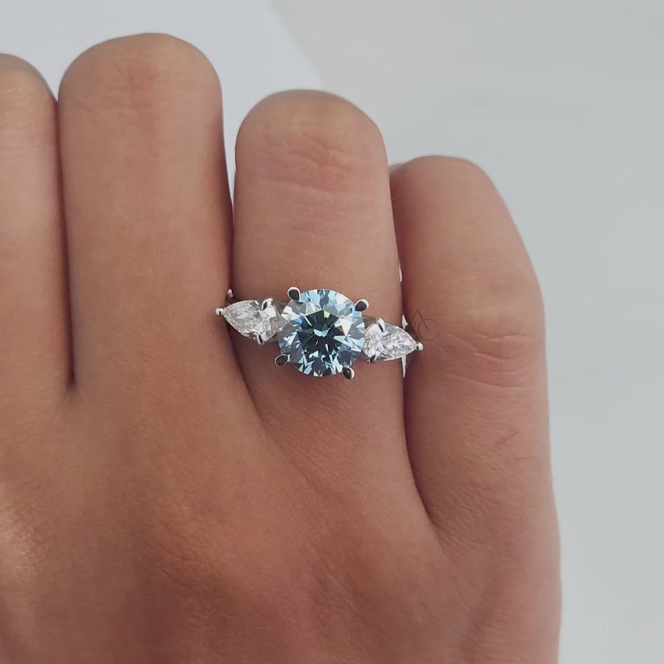360-degree view of a round blue diamond three-stone ring with pear-cut side diamonds, showcasing sparkle and intricate design.