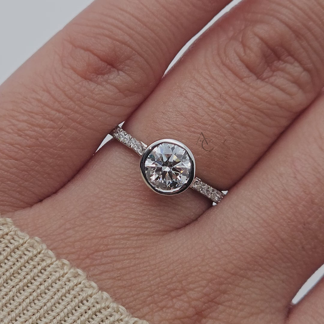 A bezel-set solitaire diamond engagement ring with a pave band in 360 view.