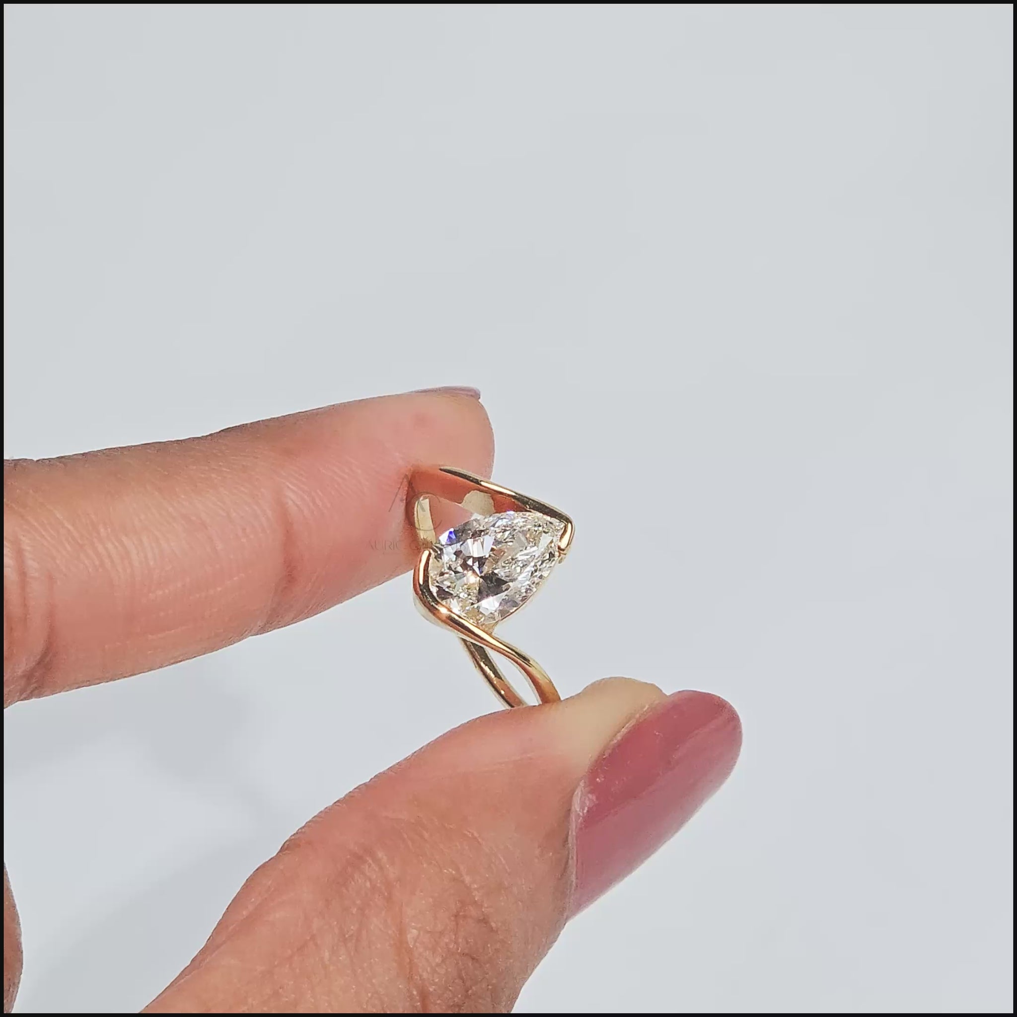Pear-shaped diamond ring in a sculptural gold setting on a stone surface.